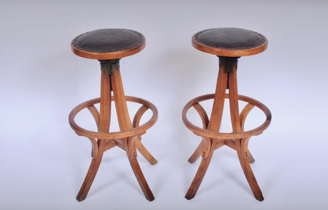 Pair of Early 20th Century Oak and Dark Brown Leather 33H Swivel Stools. Featuring a solid Oak framework,footrest, round padded vintage leather seats, cast iron mechanisms and Eiffel tower base. Sculptural. Sturdy. Comfortable.  Kindly note that