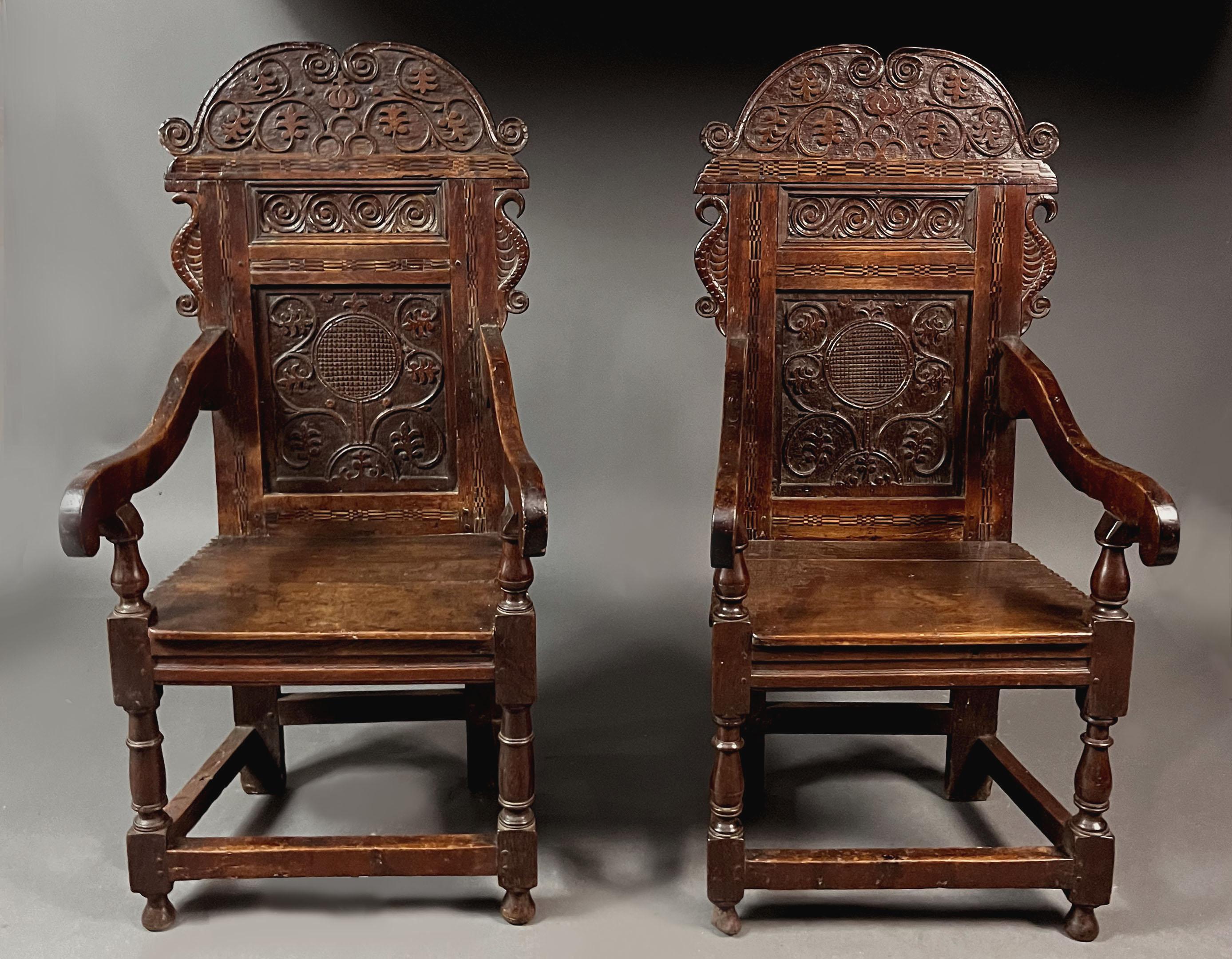 A rare pair of late 17th century oak wainscot chairs. Very striking detail: grand cresting rail with very similar carved detail to the main panel and a further smaller panel with 4 carved scrolls, well carved 'ears' and back framing with chequered