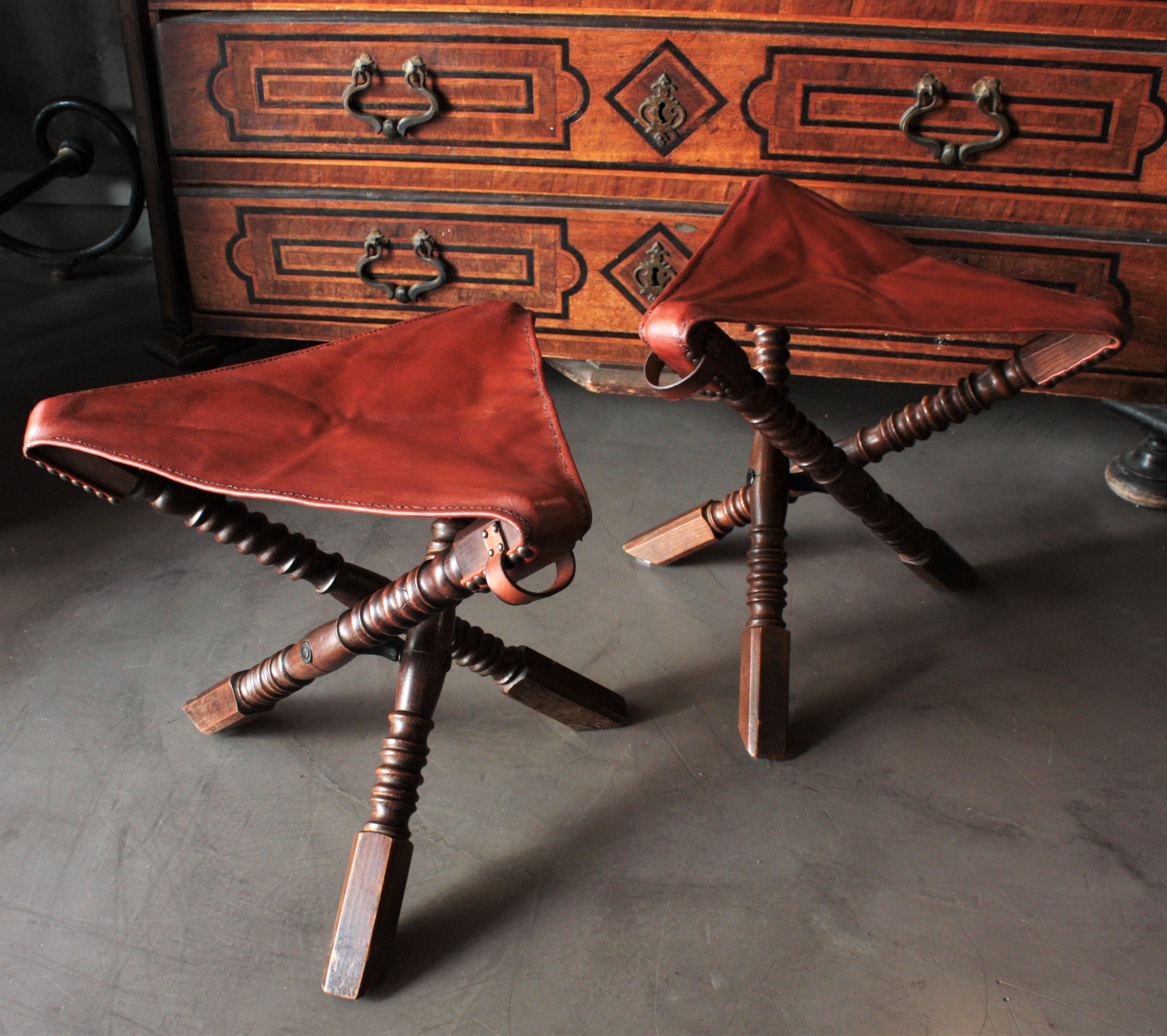 Elegant pair of turned oak Campaign tripod stools with leather folding seats. England, 1930s.
These folding stools feature a turned oak's wood tripod foldable structure. They have a leather triangle shaped seat and a leather handle in one
