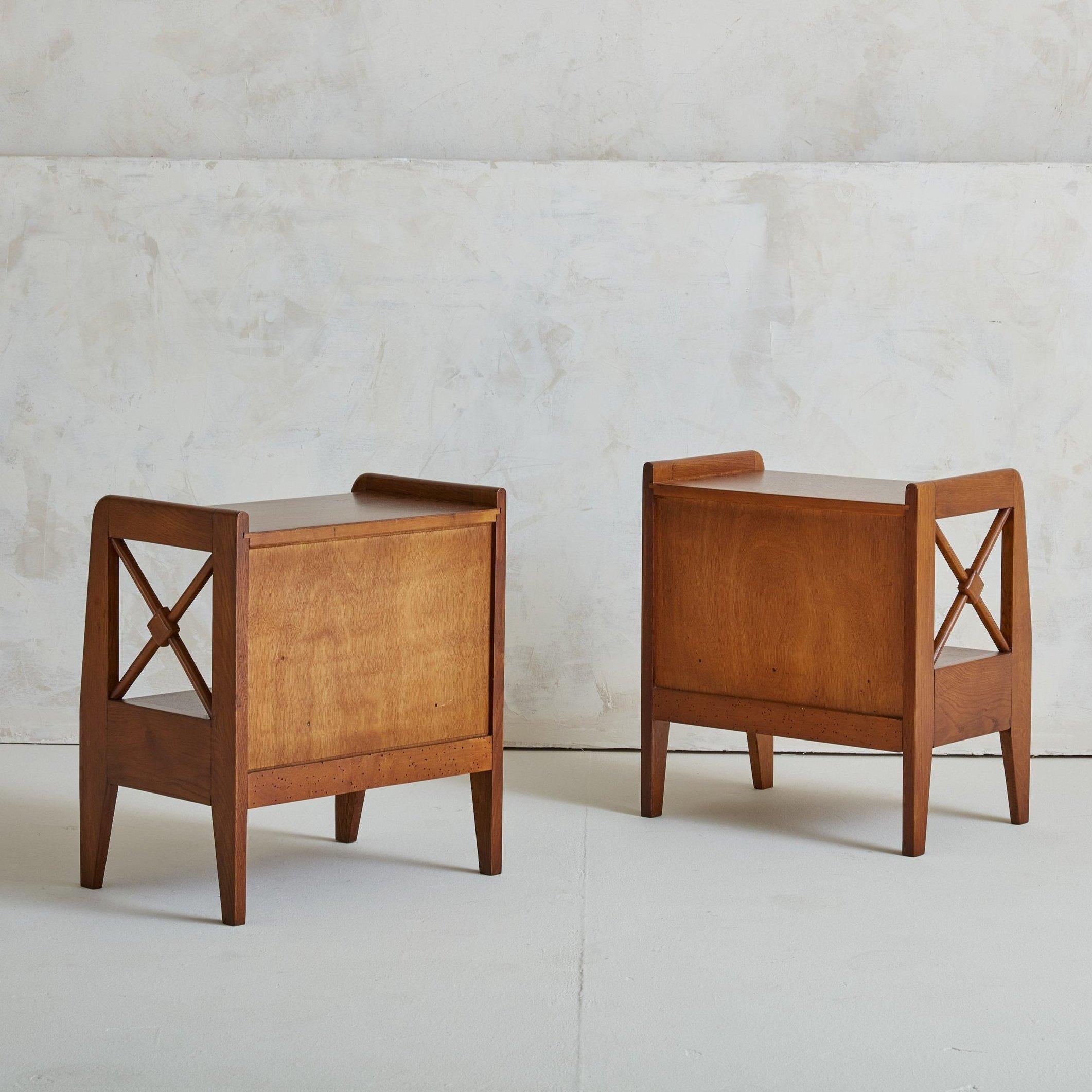 A pair of 1950s nightstands sourced in France. Crafted of oak wood, these feature decorative side stretchers and a single drawer for storage. These are inspired by forms of Jacques Adnet. These have been fully refinished and restored by our team of
