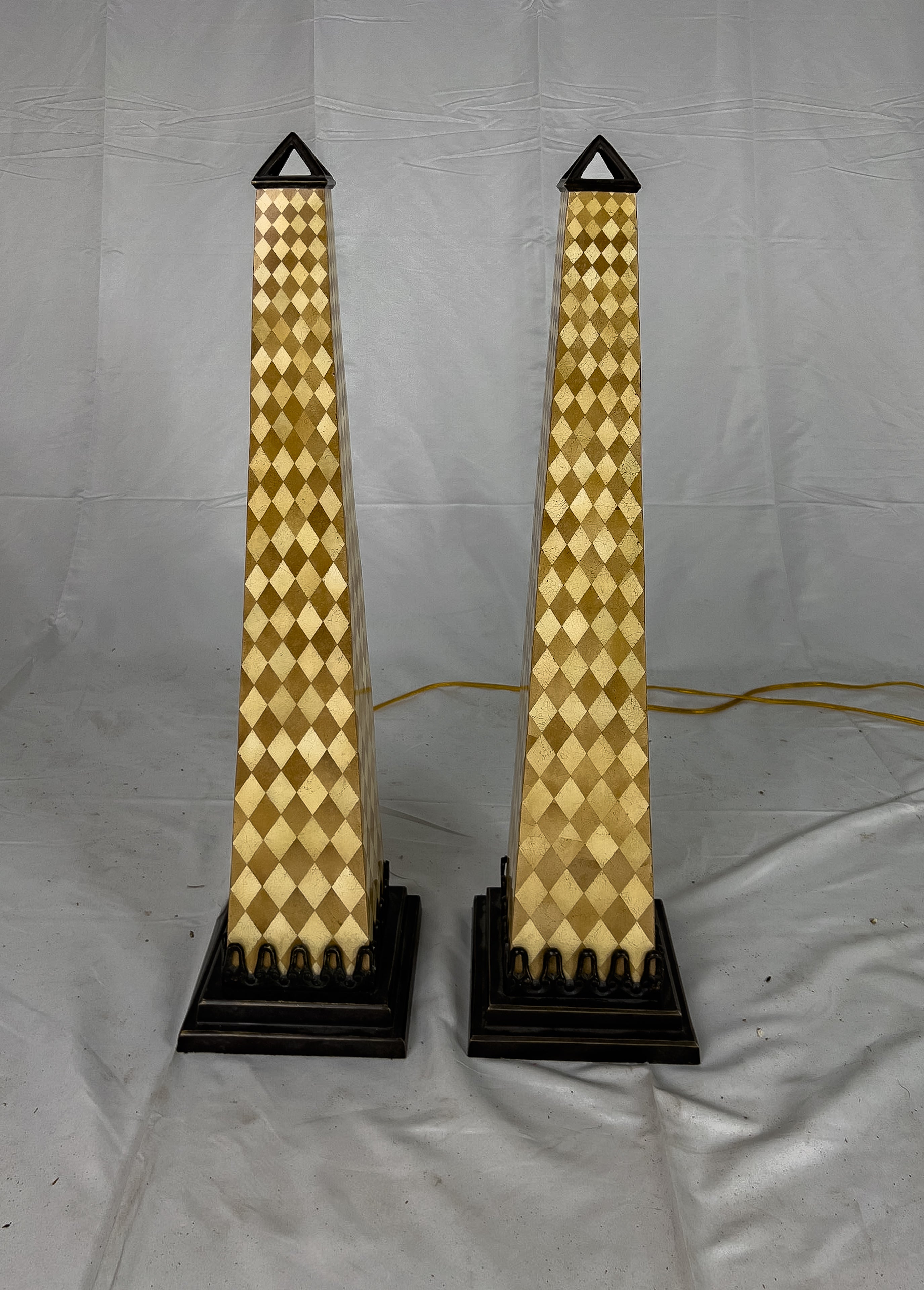 Paire de lampes de table Obélisque avec un corps en résine à motif arlequin et un capuchon et une base en métal de couleur bronze. Cette lampe est dotée d'une fiche de type A et peut atteindre 120 V (norme américaine).