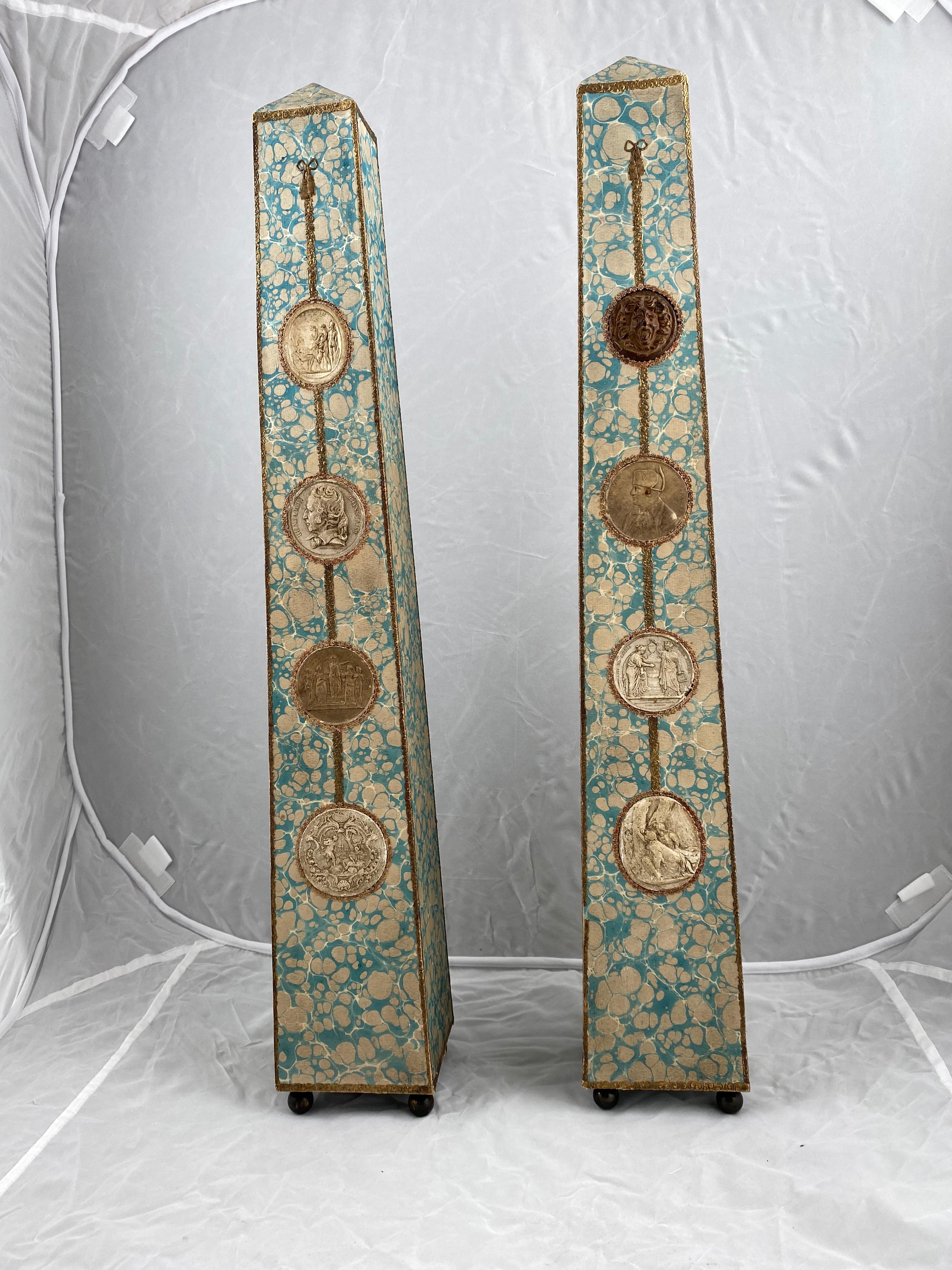 A fantastic and rare pair of obelisks, Empire, made circa 1810. They are made of wood and covered with printed paper and seals depicting among other things Napoleon. The obelisks are standing on round brass feet. 

There is great feeling to the