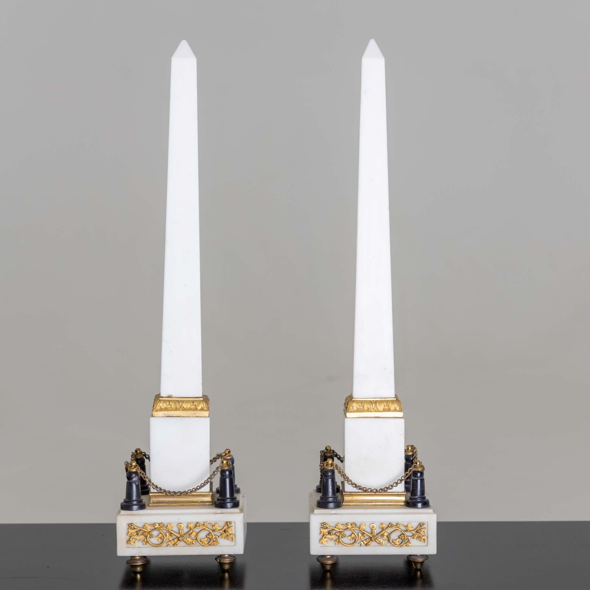 Pair of white marble obelisks with fire-gilded bronze mounts.