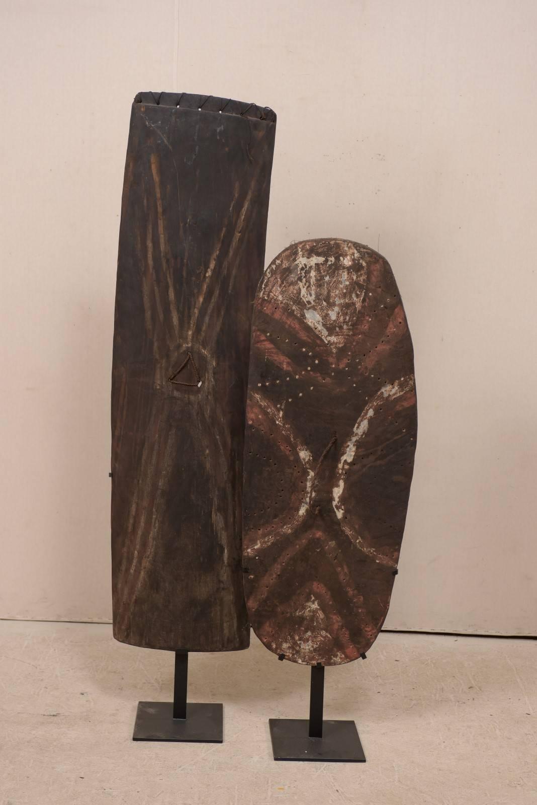 A pair of Papua New Guinea wooden shields on custom stands from the mid 20th century. These oceanic war shields were not only created for protecting oneself for tribal warfare, but also in ancestral and ritual worship. They are adorn in various