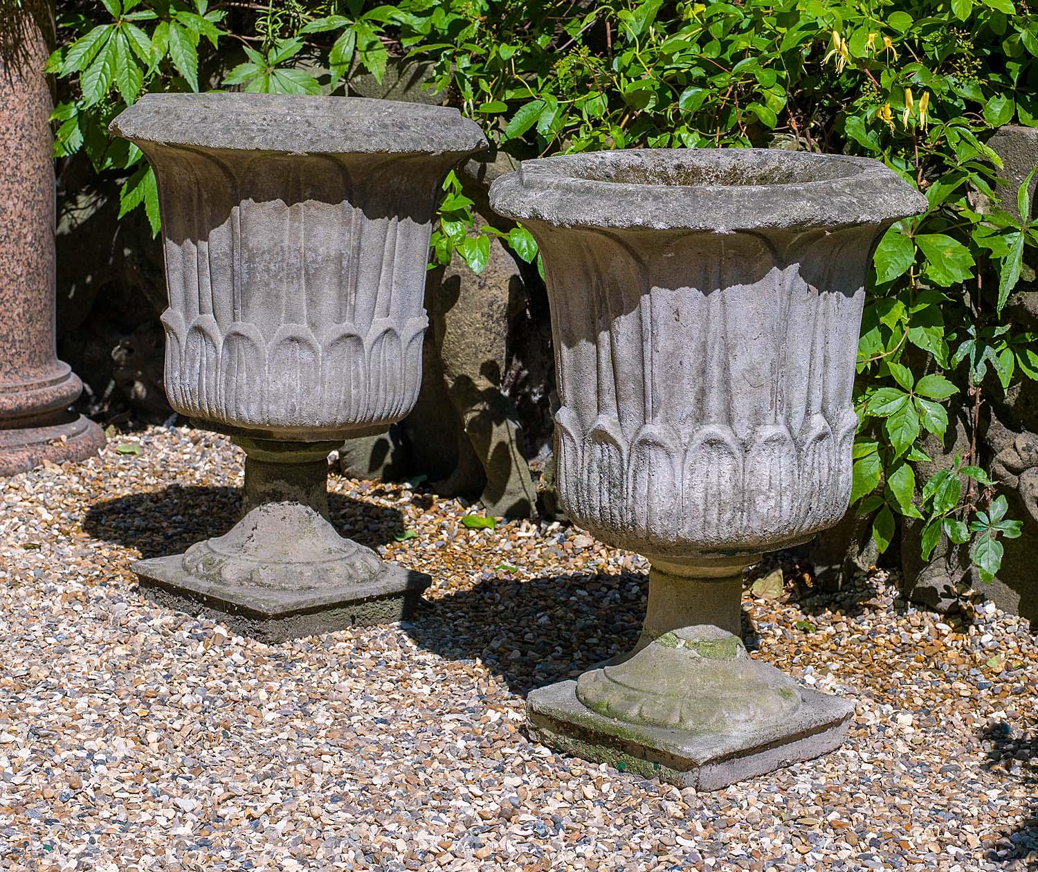 A pair of octagonal mid-20th century reconstituted stone urns in the neoclassical style with carved foliate detail raised on small socles, English, mid-20th century.