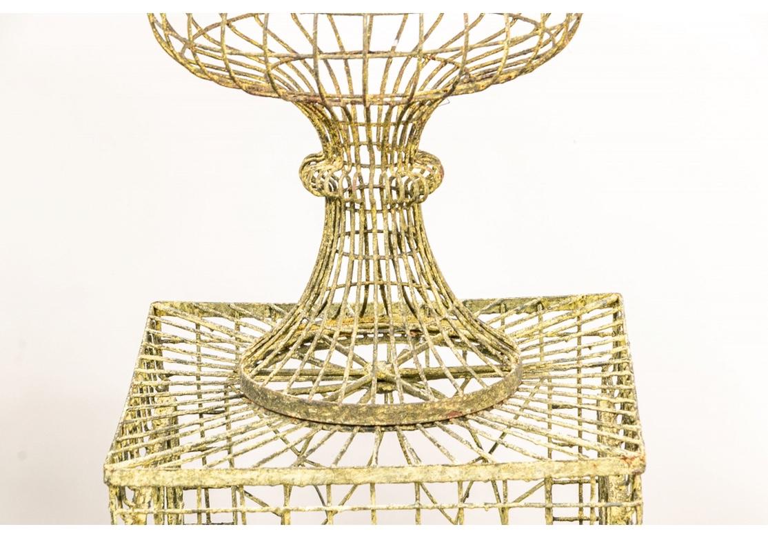 Tall open wire footed urns in old yellow paint, mounted in one piece with the open wire pedestal bases. The pedestals with openwork ovals on the sides and starburst tops.
Measures: Total height 53 1/2