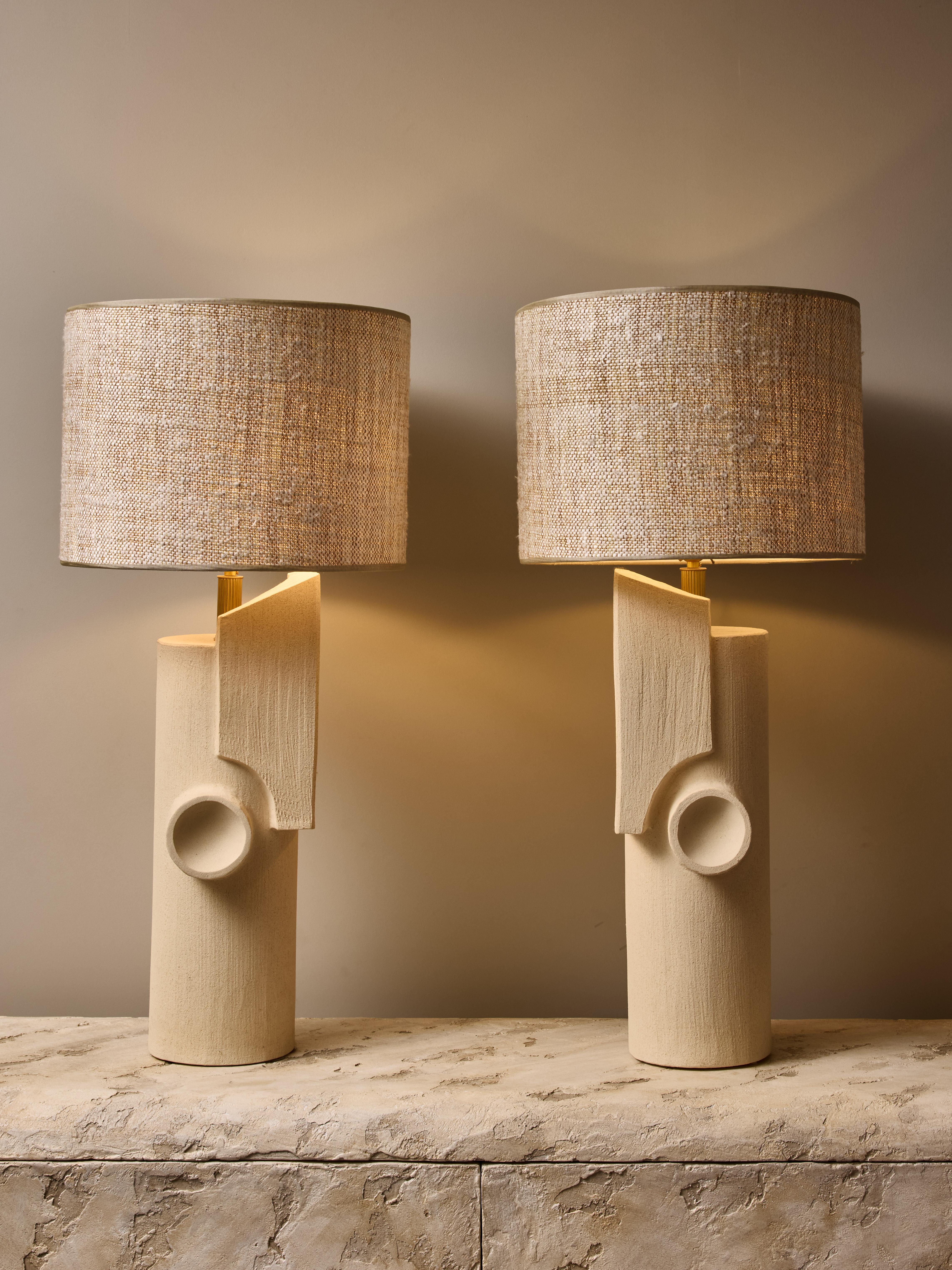 Pair of ceramic table lamps by the talented french contemporary artist Olivia Cognet.

These large tubular shape lamps have mirrored, almost book end, design of sharp geometrical shapes, brass hardware and topped with a custom lampshade.

Stamped on
