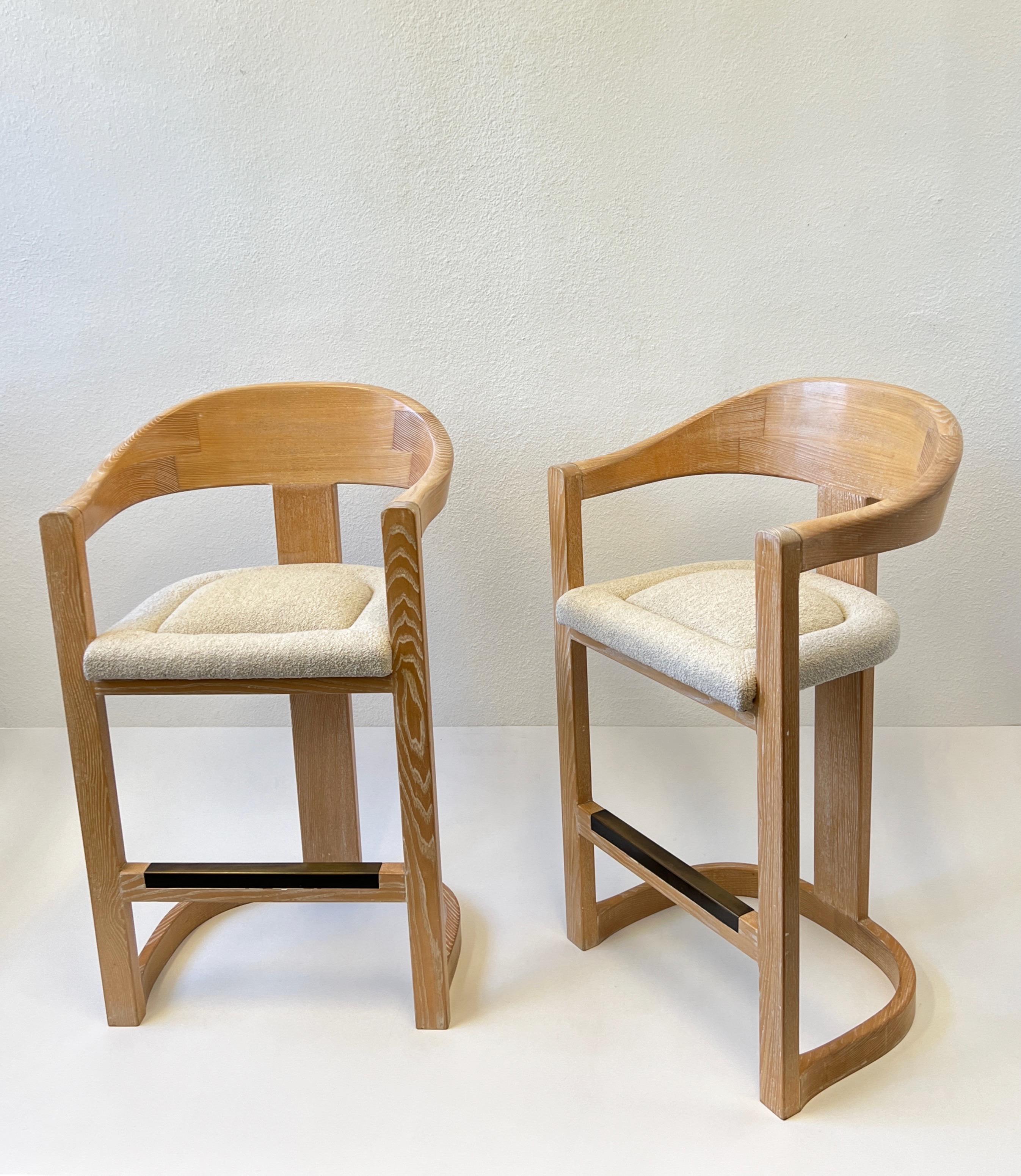 Pair of glamorous 1980’s “Onassis”Barstools by Karl Springer. 
Constructed of whitewashed dowelwood and aged bronze footrests, the seats are newly recovered in Italian natural sheep wool boucle fabric. 
The frames are in original vintage