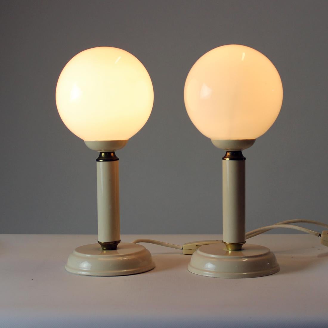 Ensemble de deux élégantes lampes de table, produites en Tchécoslovaquie dans les années 1970. Les lampes reposent sur une base métallique en glaçure de couleur crème avec des détails en laiton. Le bouclier est fabriqué à partir d'un verre opalin