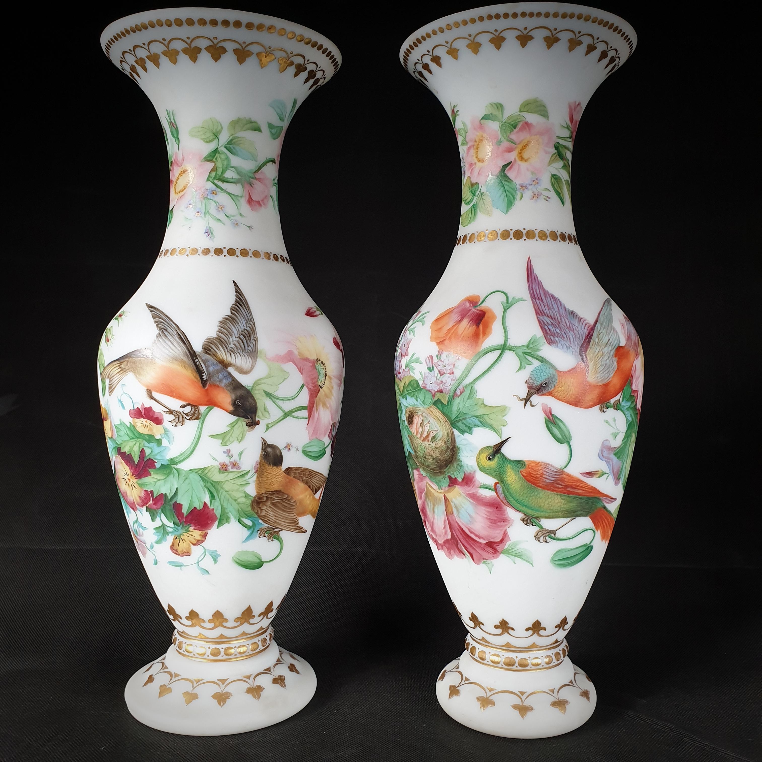 Paire de vases opalins en forme de trompette. De magnifiques motifs floraux peints à la main dans une variété de couleurs et de vibrants oiseaux prenant soin des poussins et gardant leur nid ornent ce couple de mariés. Les coins et les jantes ont