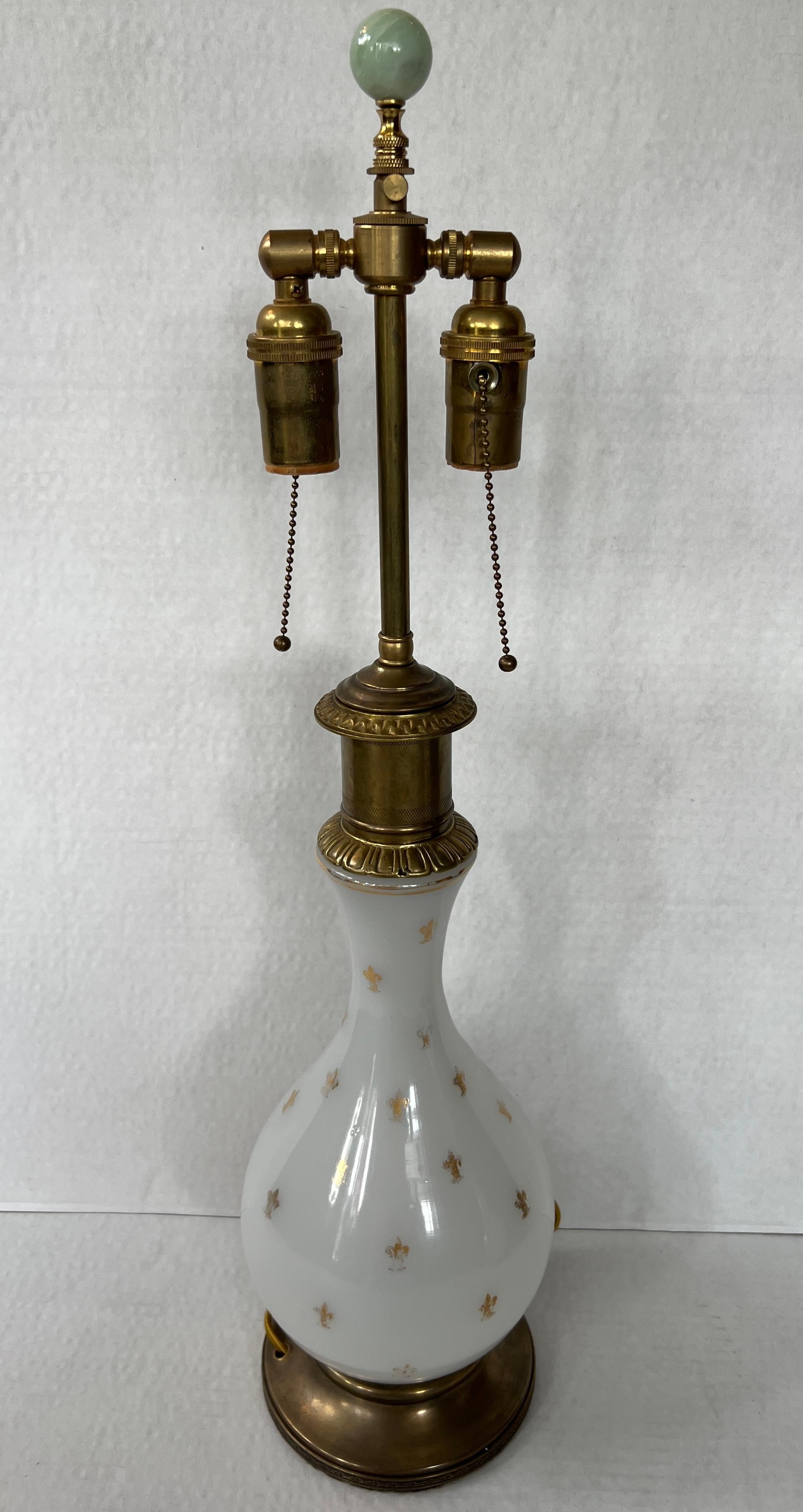 A pair of 1920s table lamps adorned with opaline glass and distinguished by gilded Fleure de Lis detailing.