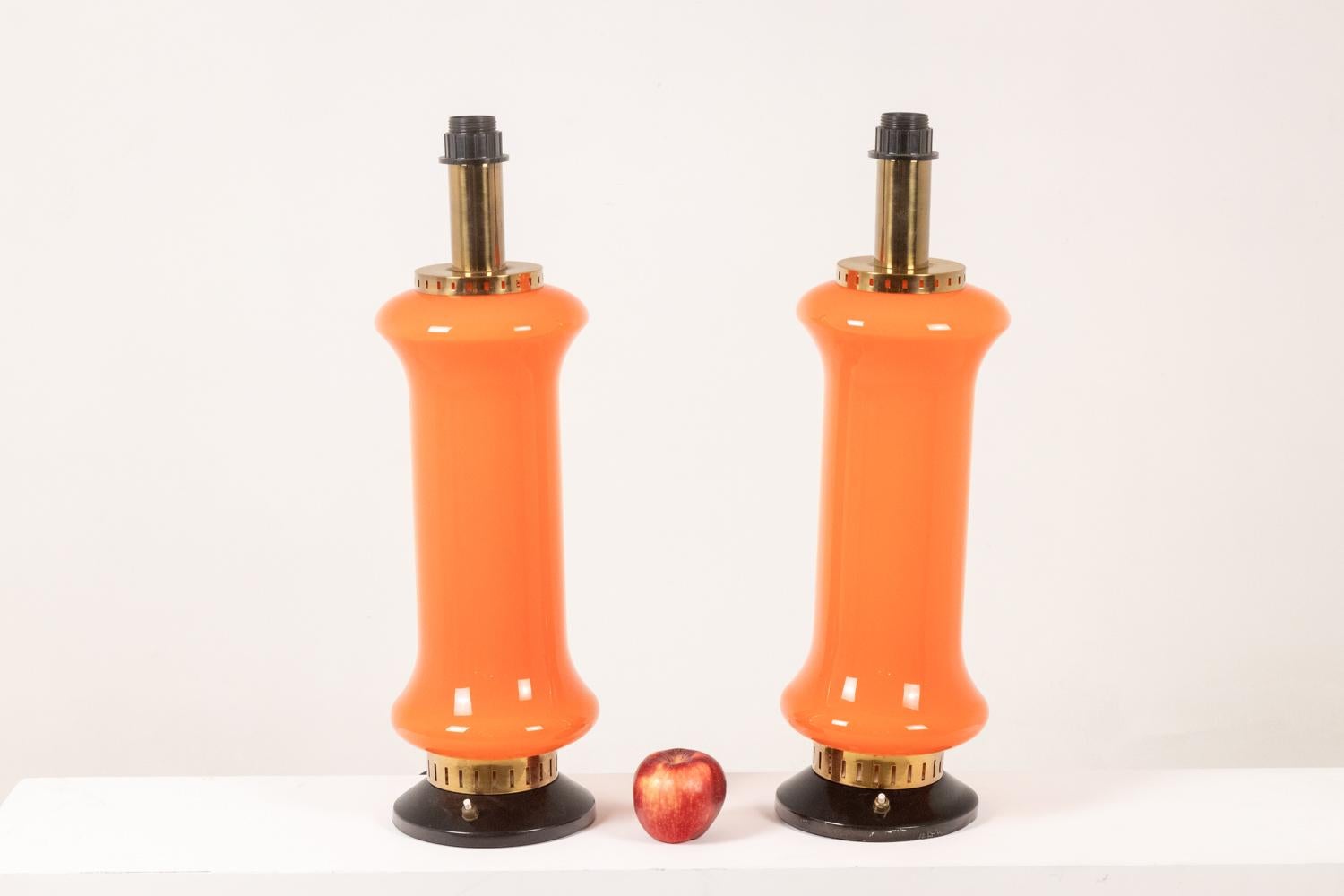 Pair of cylindrical lamps, the body in orange glass and the round black lacquered base, the ring and the top of the lamp in gilded brass. Push button that turns on the bulb inside or the bulb outside, or both.

Italian work realized in the