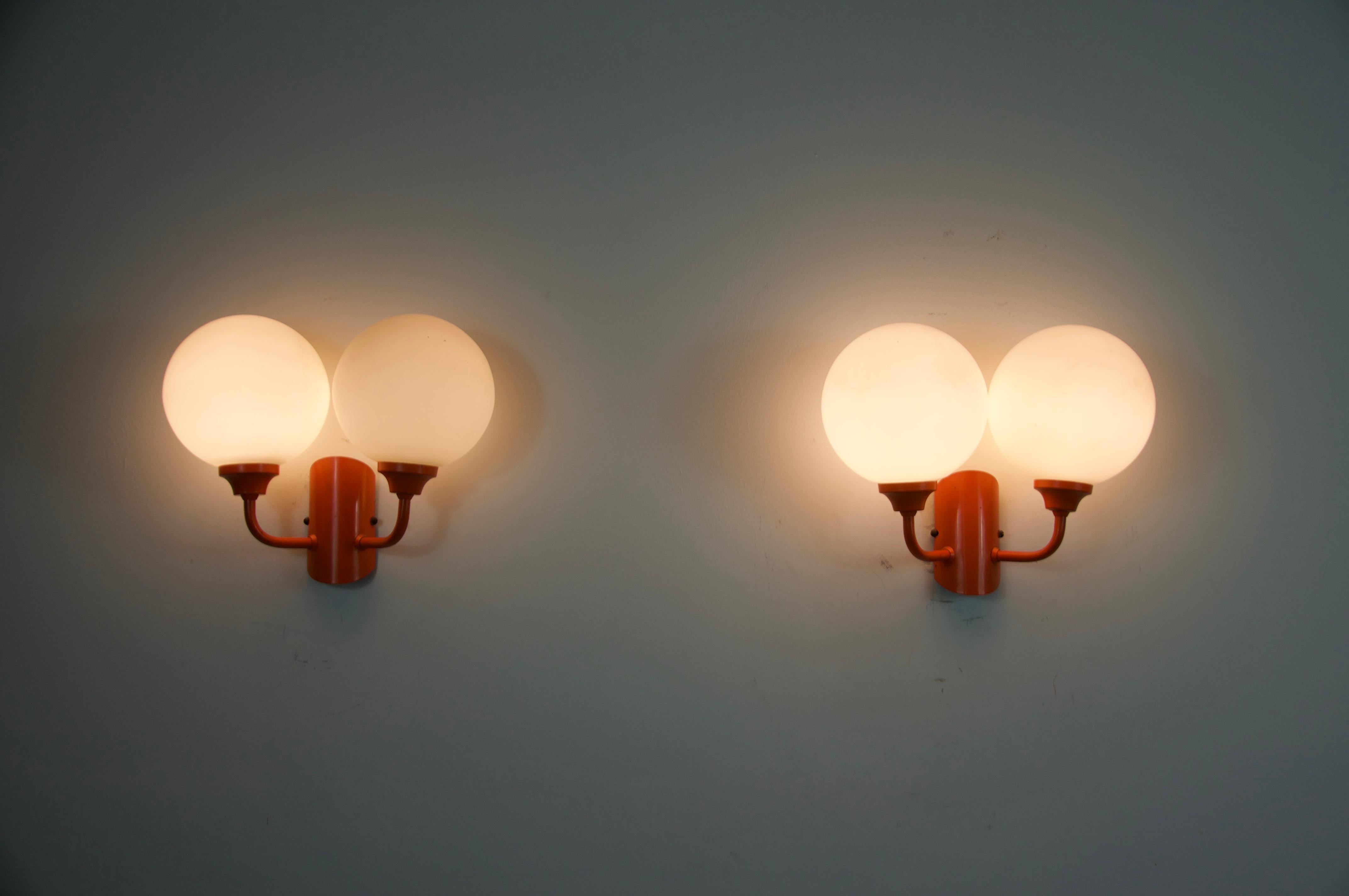 Cette paire d'appliques en métal orange et verre opalin a été fabriquée en Allemagne dans les années 1960. Chaque lampe présente deux bras élégamment incurvés, se terminant par des abat-jours sphériques en verre opalin qui renferment les ampoules.