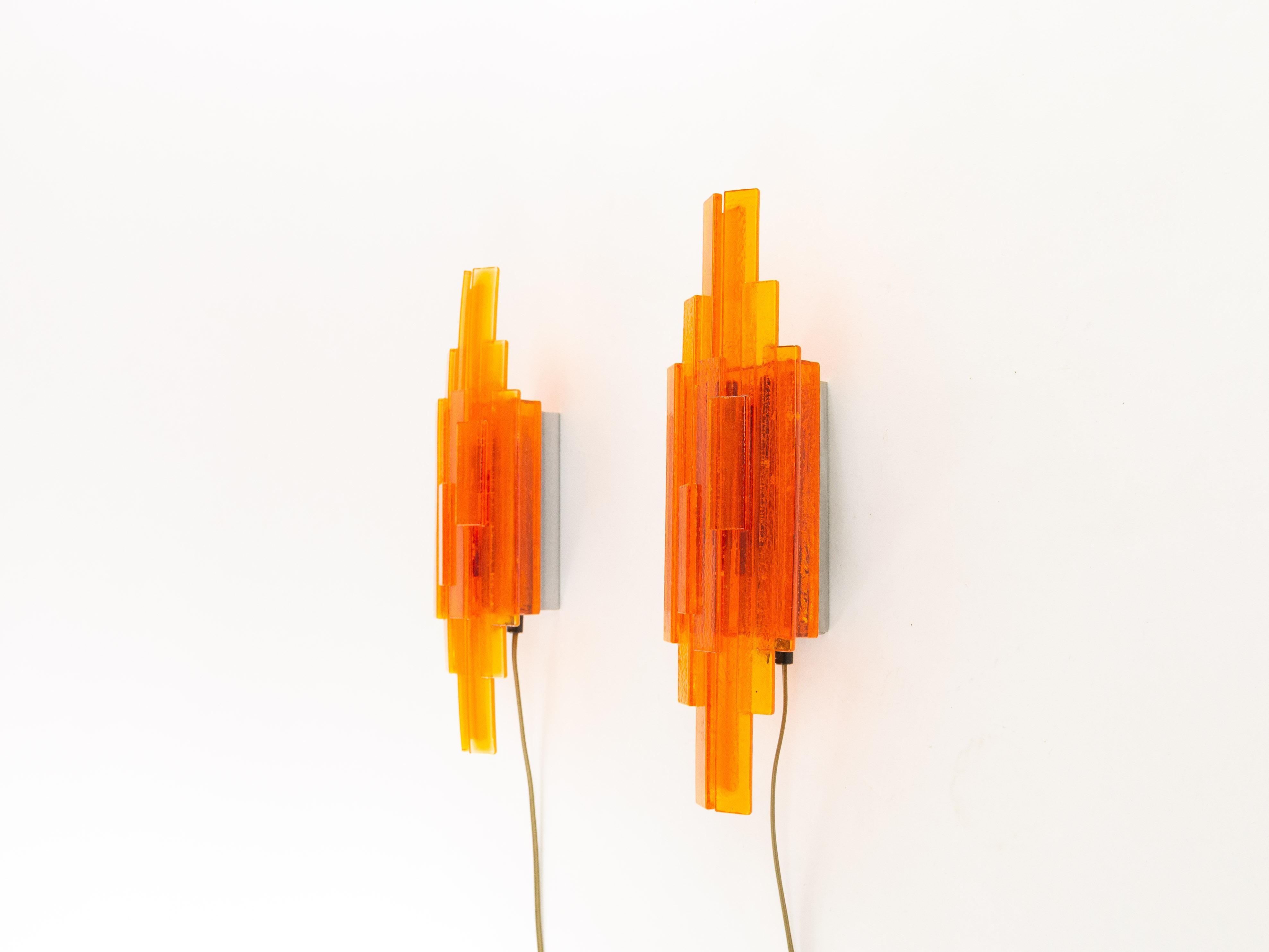 A pair of orange handmade acrylic wall lamps. The sconces were designed by Claus Bolby and manufactured by his own company, Cebo industry. By experimenting, Bolby discovered a technique allowing him to introduce bubbles into the acrylic, which adds