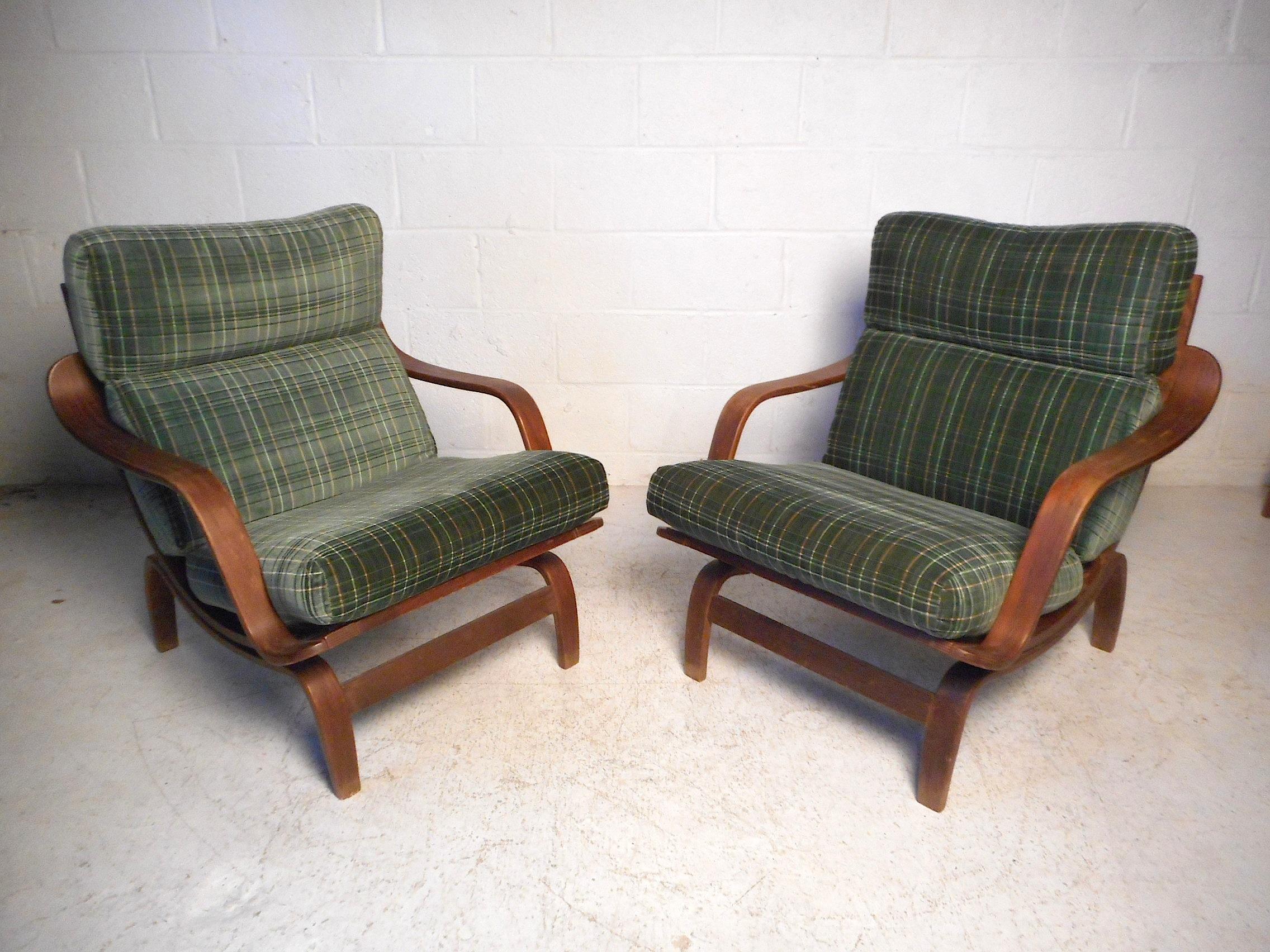 This stylish pair of midcentury lounge chairs feature a molded wood frame, contoured armrests, and comfortable seat cushions covered in a green plaid upholstery. Please confirm item location with dealer (NJ or NY).