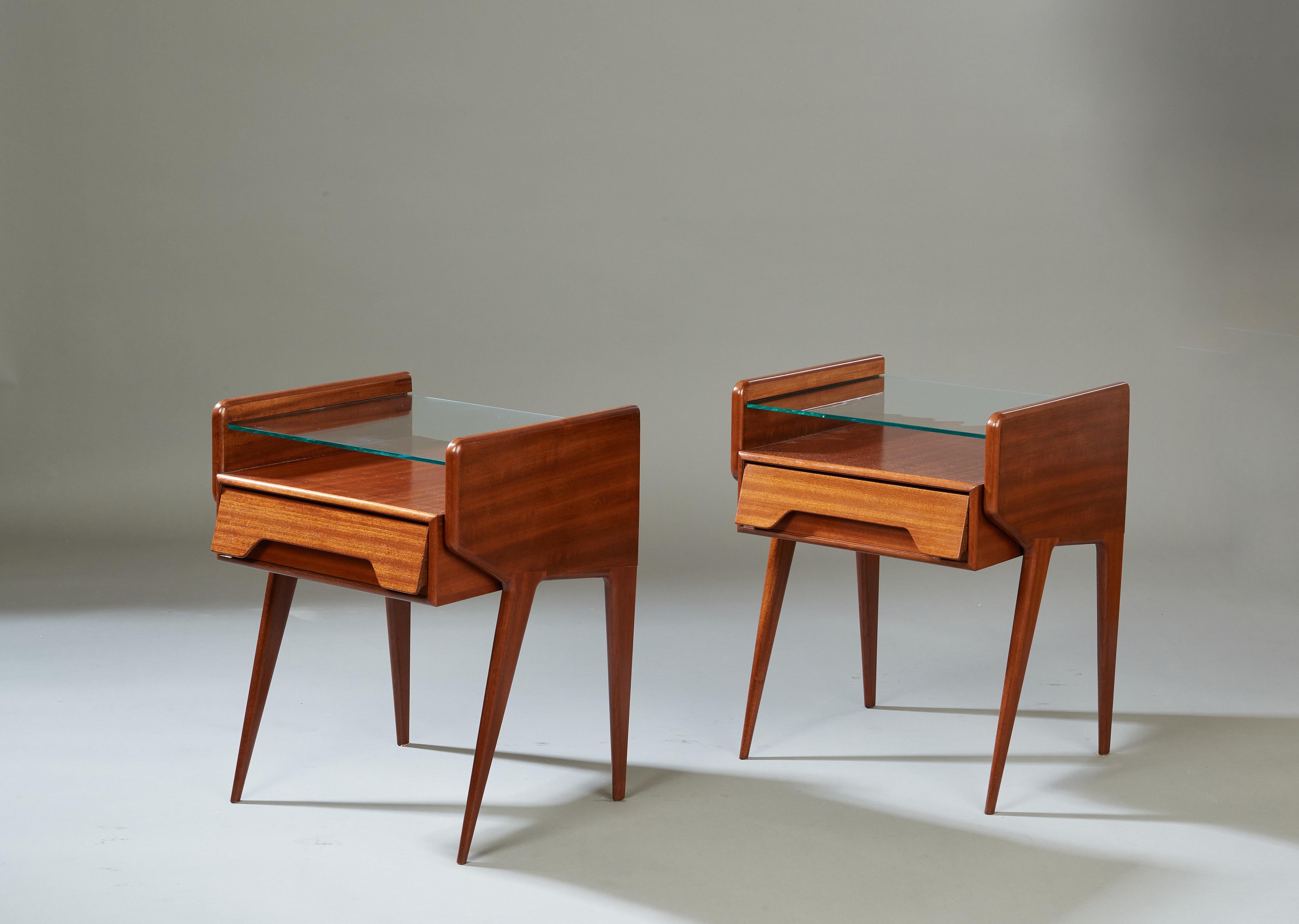 Italie, années 1950 

Une paire dynamique de tables de chevet modernistes à la manière d'Ico Parisi, en acajou poli avec un grain vibrant d'œil de tigre. Un corps fluide et ailé aux bords arrondis soutient une étagère en verre flottante et un tiroir