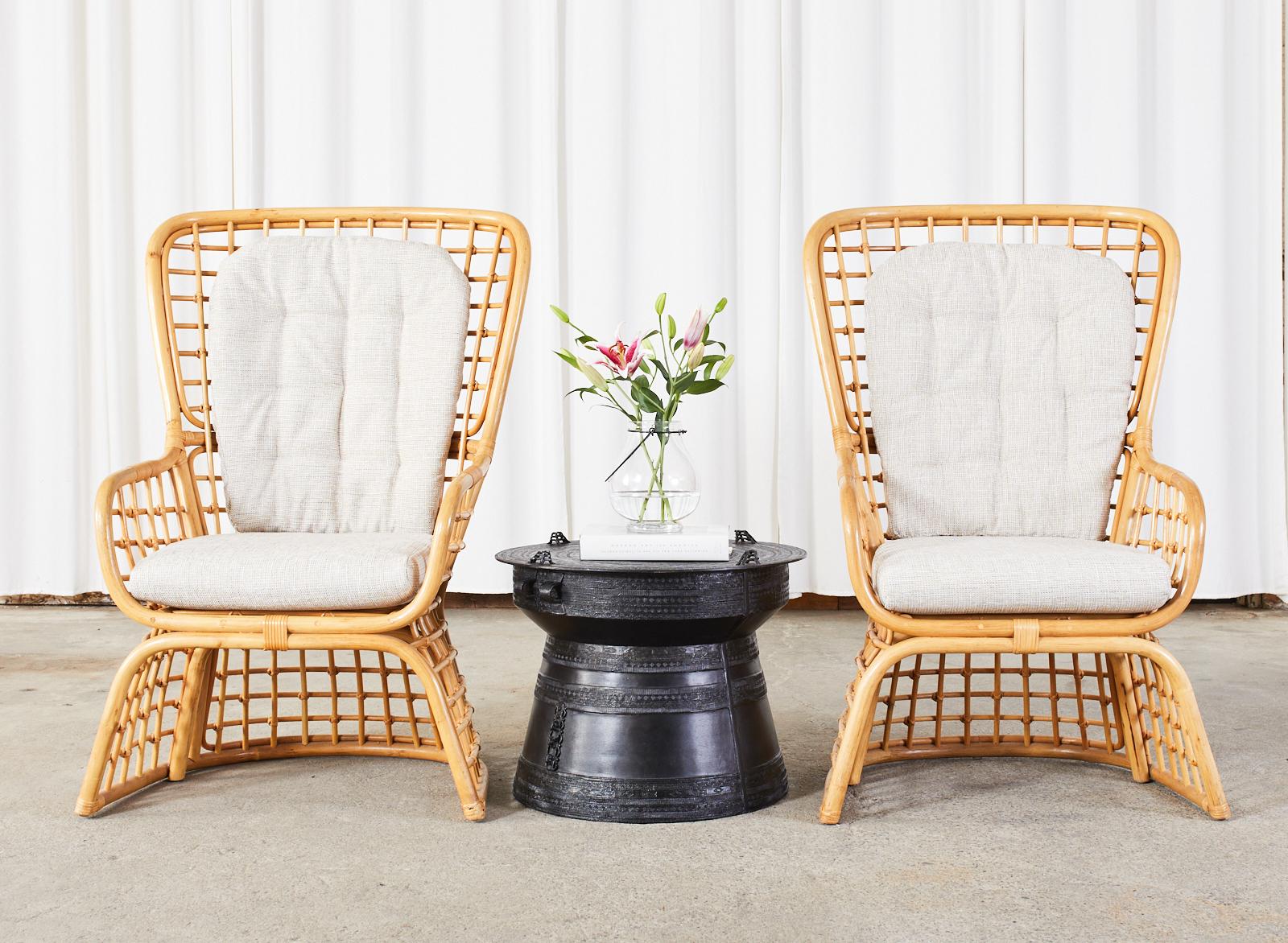 Mid-Century Modern pair of high back wing chairs constructed from rattan and wicker. Made in the organic modern style featuring a large bent rattan frame with open fretwork geometric grid design. The chairs have a waisted or hourglass form with a