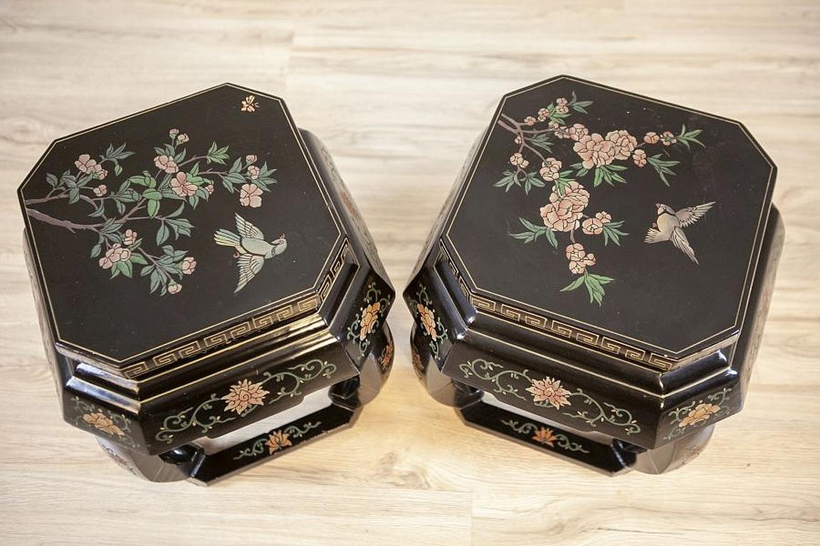 Pair of oriental tables from the early 20th century

Pair of black tables with tops decorated with genre scenes. Both pieces are circa the 1st of the 20th century. The arch-like legs are supported at the bottom by stretchers, which are also