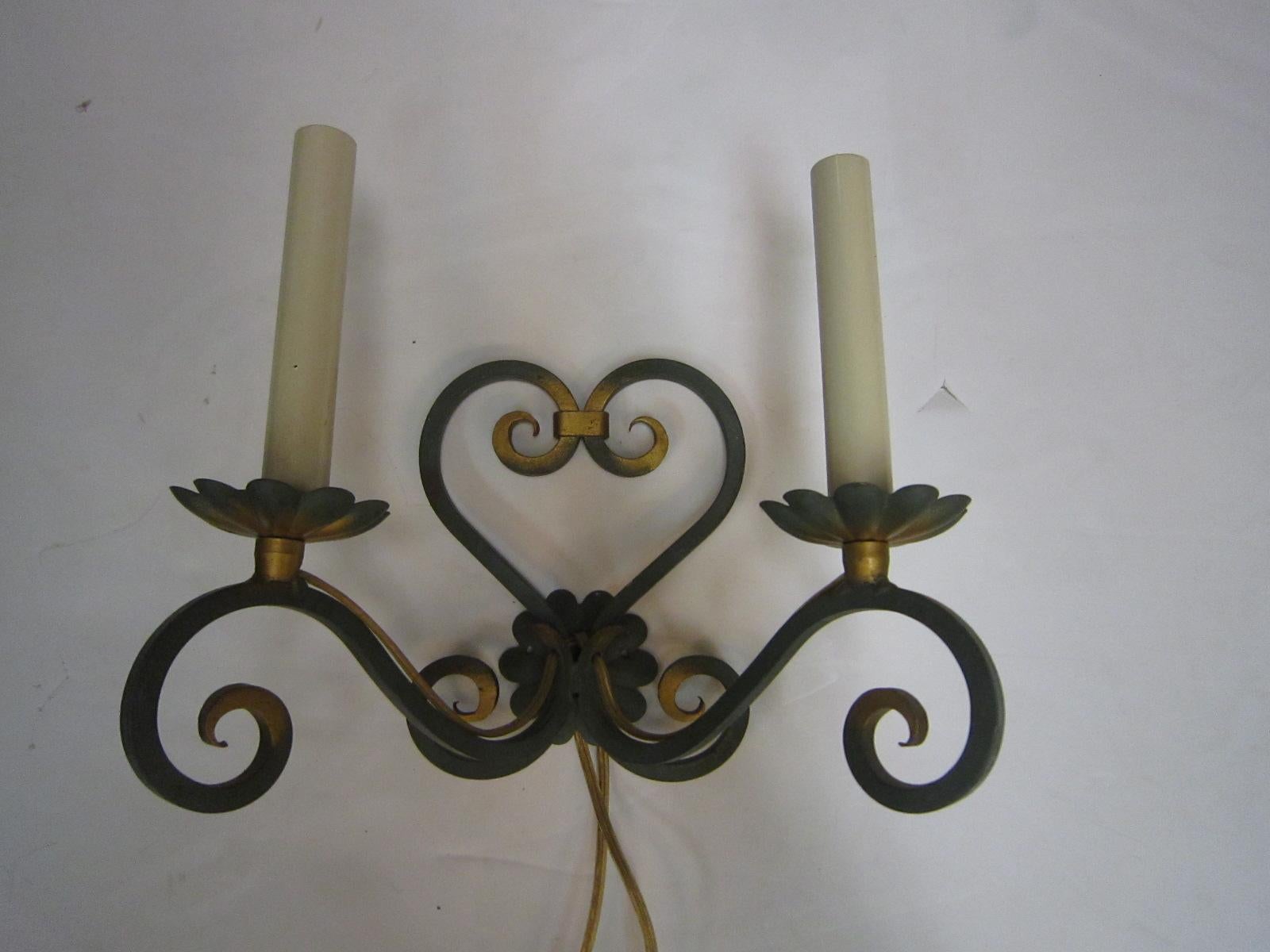 A lovely pair of period French hand forged iron sconces, double arms with hand painted gilt accents, heart shaped back plate, flower bobeches and scroll decoration. 
The candleholders can be made shorter if need be and the green patina can be