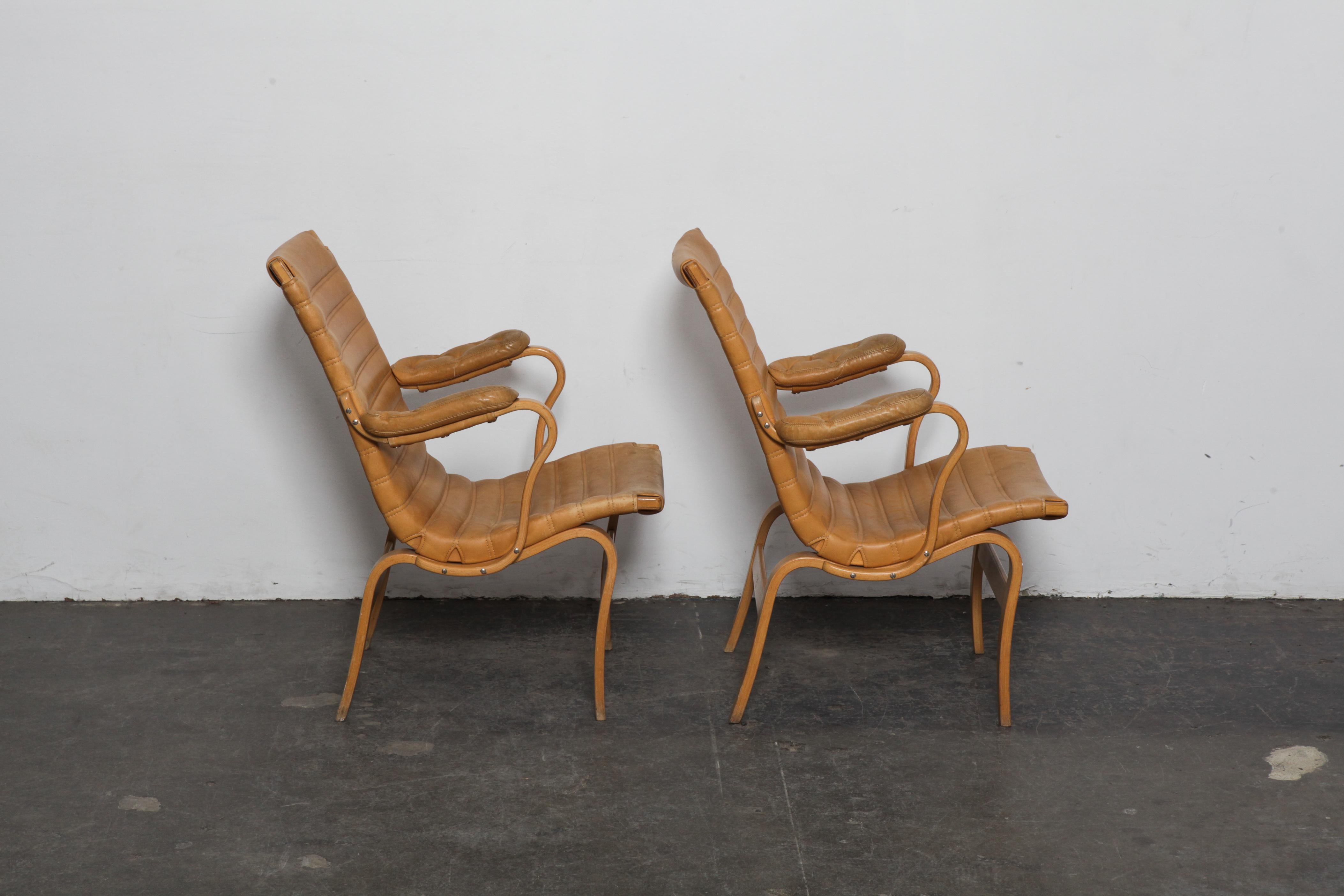 Paar Bruno Mathsson 'Eva'-Stühle aus Buche und originalem, horizontal getuftetem hellbraunem Leder, Schweden, 1960er Jahre, hergestellt von Dux. Leder und Stuhlrahmen sind im ursprünglichen, unberührten Zustand, weisen aber Patina und Abnutzung auf.