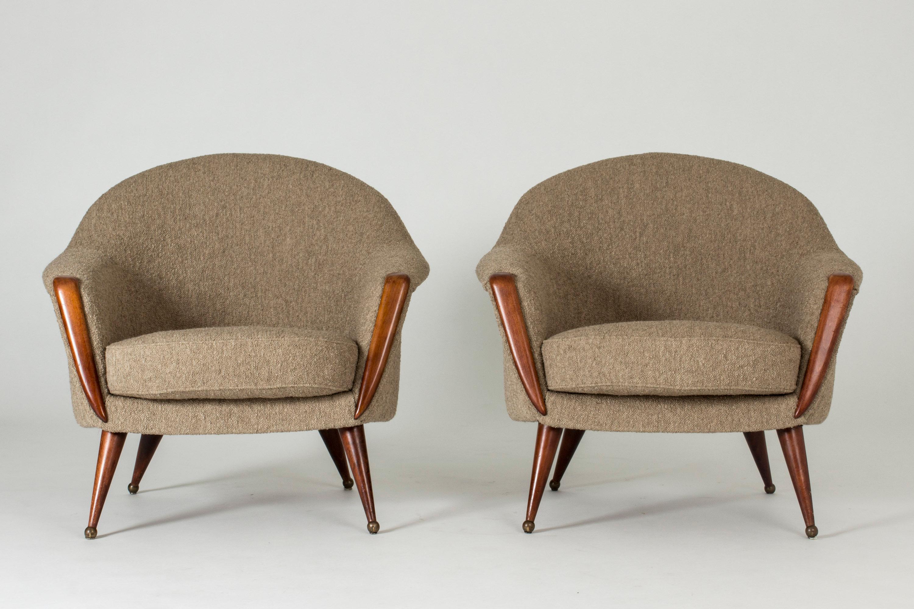 Pair of “Orion” lounge chairs by Folke Jansson, in a rounded design. Brown wooden legs and details on the front, round brass ball feet. Bouclé upholstery.