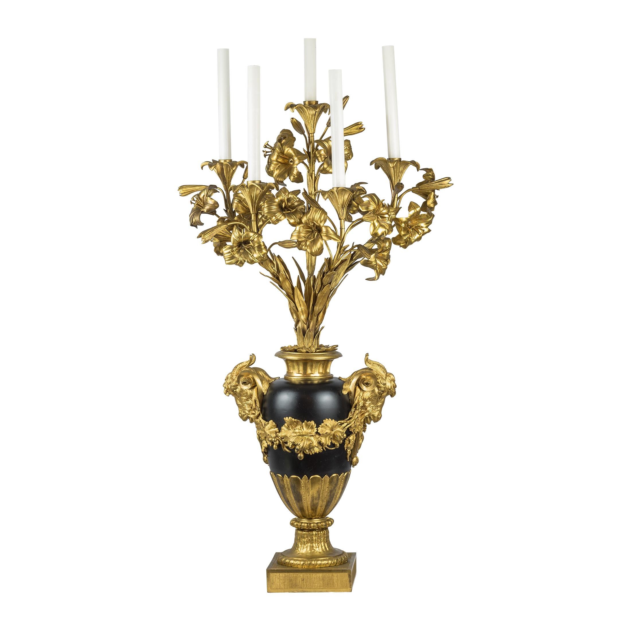 Une paire de candélabres de qualité en bronze doré à cinq lumières avec des bras floraux et des poignées en forme de tête de bélier sur une urne en porcelaine avec une vigne tout autour et des poignées en forme de tête de bélier, le tout culminant