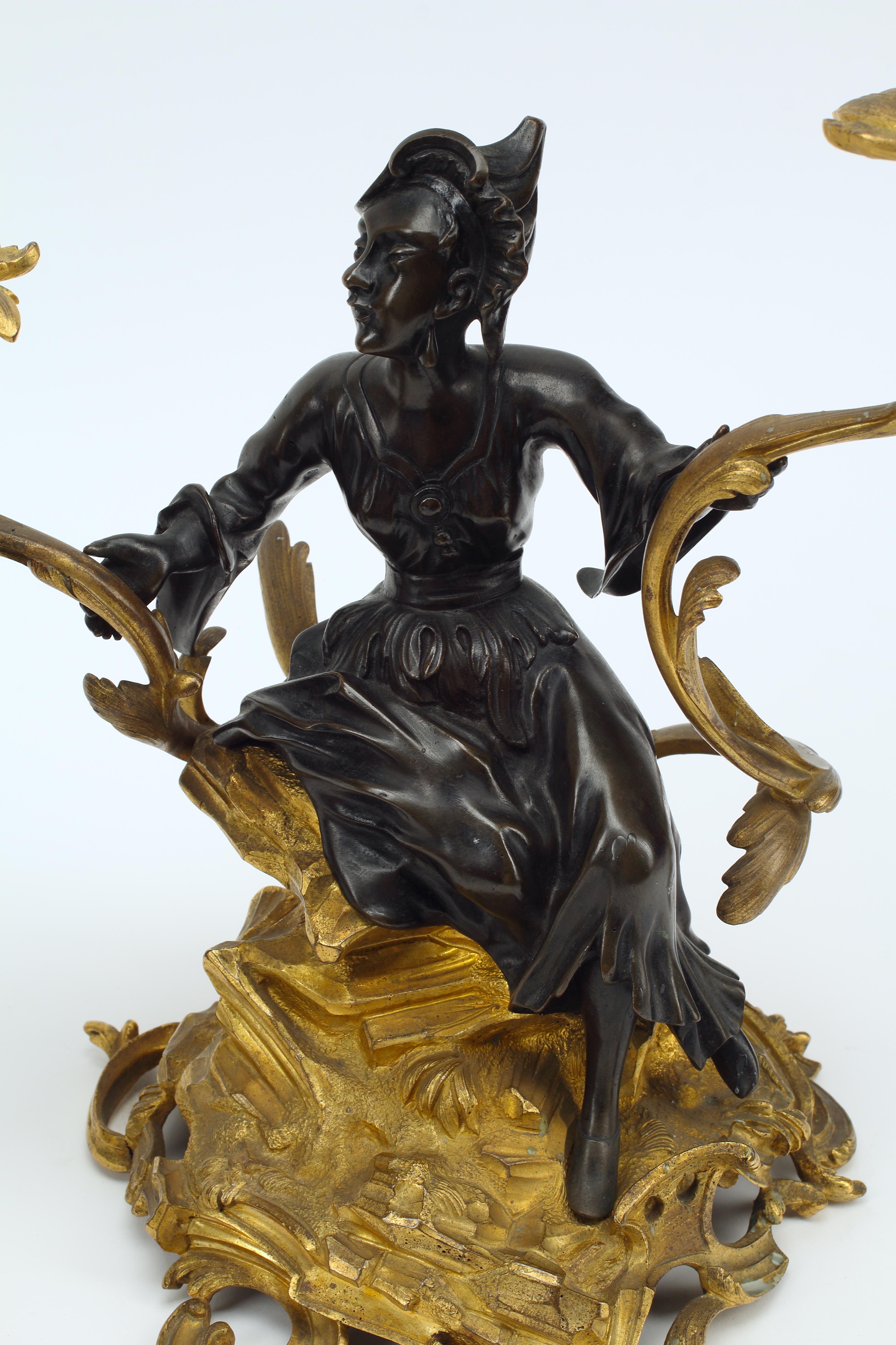 A fine example of French ormolu and patinated bronze craftsmanship, this pair of figural candelabras are a stunning example of the Chinoiserie style. Each figure is crafted in patinated bronze, likely an effort to resemble black lacquer, and sitting