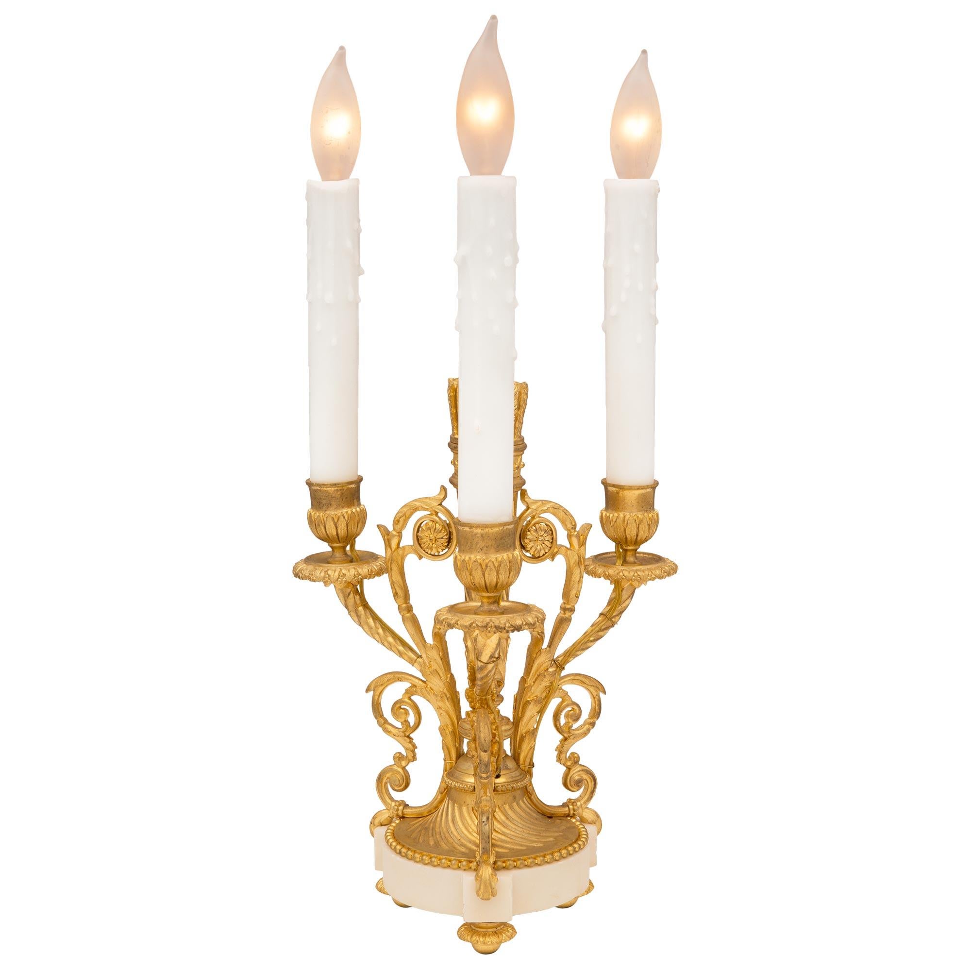 Ein schönes Paar französischer Kandelaber aus dem 19. Jahrhundert aus Louis XVI Ormolu und weißem Carrara-Marmor. Jede Leuchte wird von einem feinen, runden Sockel aus weißem Carrara-Marmor mit eleganten, topieförmigen Füßen getragen. Die