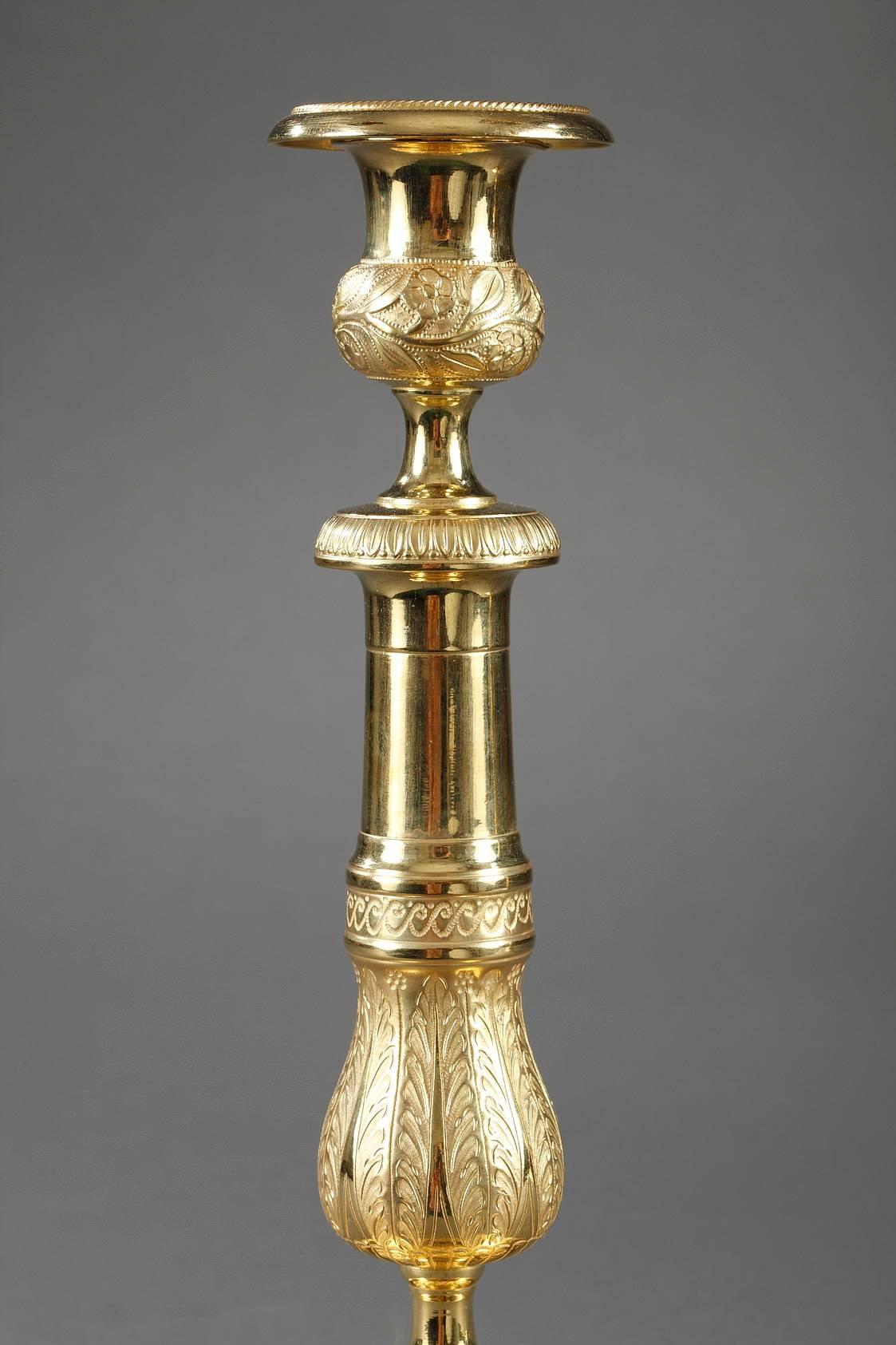 Pair of candlesticks in gilded and sculpted bronze. The stem is adorned with a frieze of Greek waves that separate the upper, polished part from the lower part that is richly decorated with palmettes, small flowers, and gadrooning. It is topped by a
