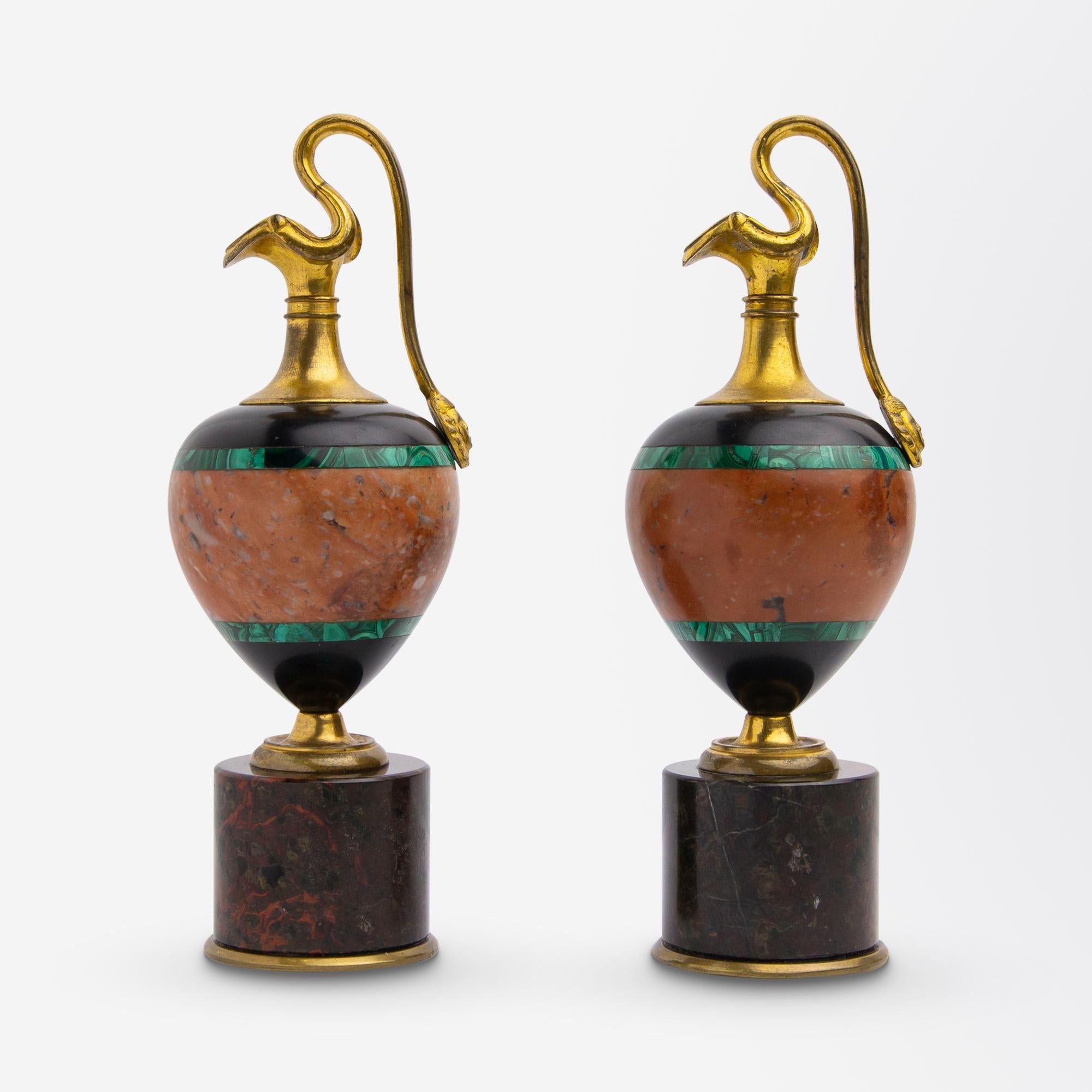 This pair of Grand Tour era ewers are in the 'oinochoe' shape and date to circa 1870. The pair are miniature in size and comprise of ormolu (gilt bronze), malachite, onyx and hardstone. The pair are ornamental and not intended for use, being just 14