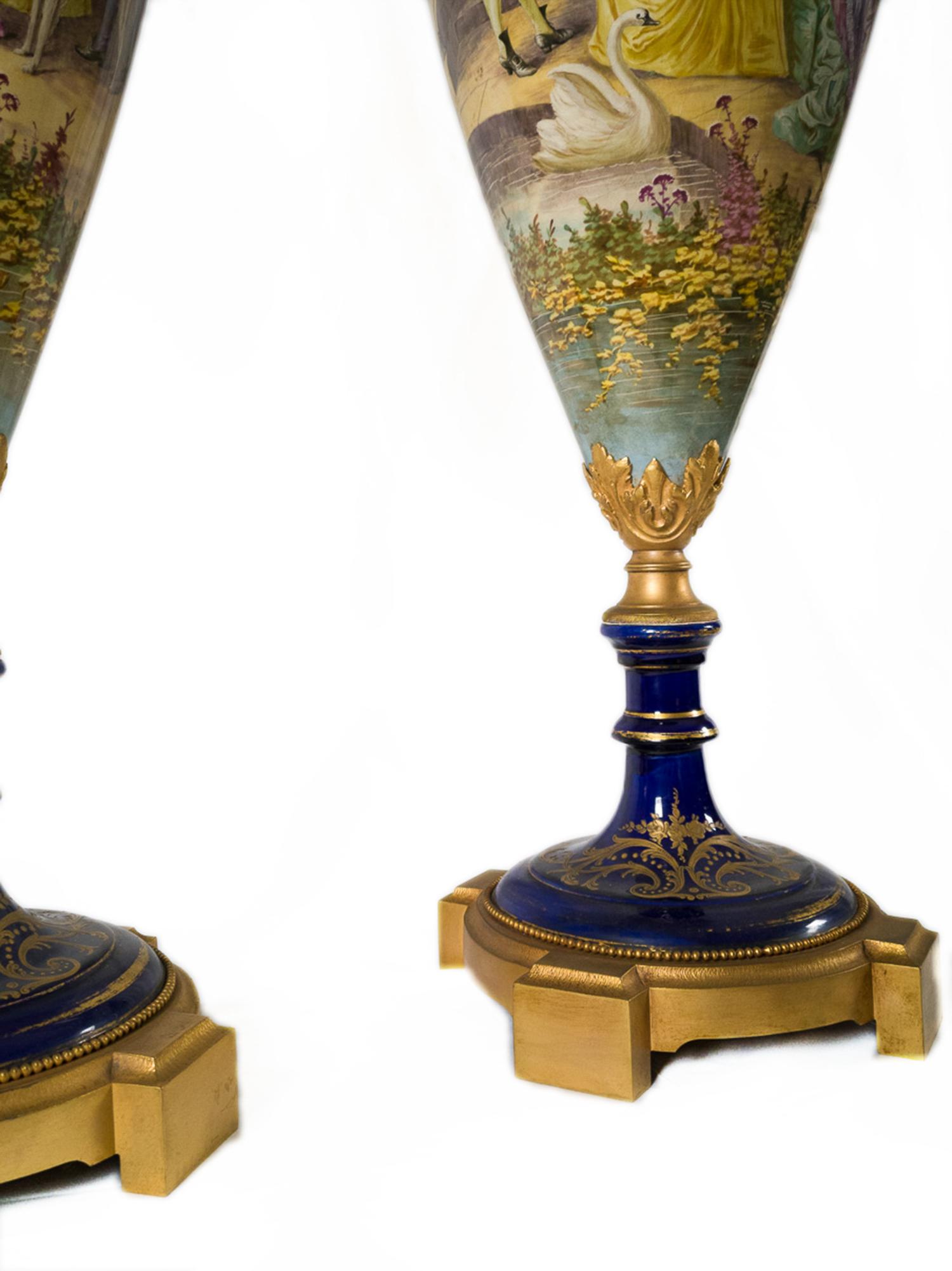 Coppia di vasi in porcellana blu cobalto montati su ormolu di Sèvres con supporti in bronzo dorato, decorati con fiori in smalto oro rococò e volute floreali policrome, decorazione galante nel rigonfiamento centrale con scena palaziale dipinta a