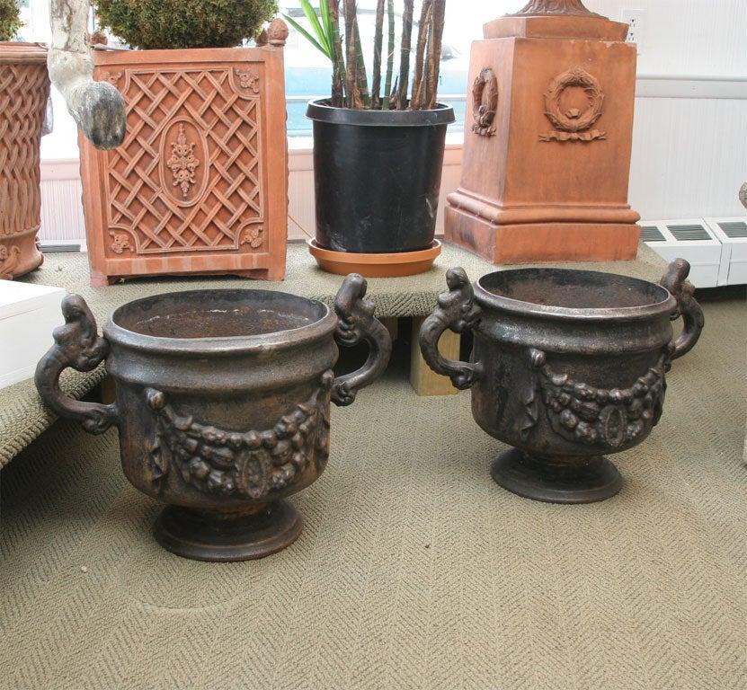 Black cast iron urns with beautiful mermaid handles and garland decor on the body.