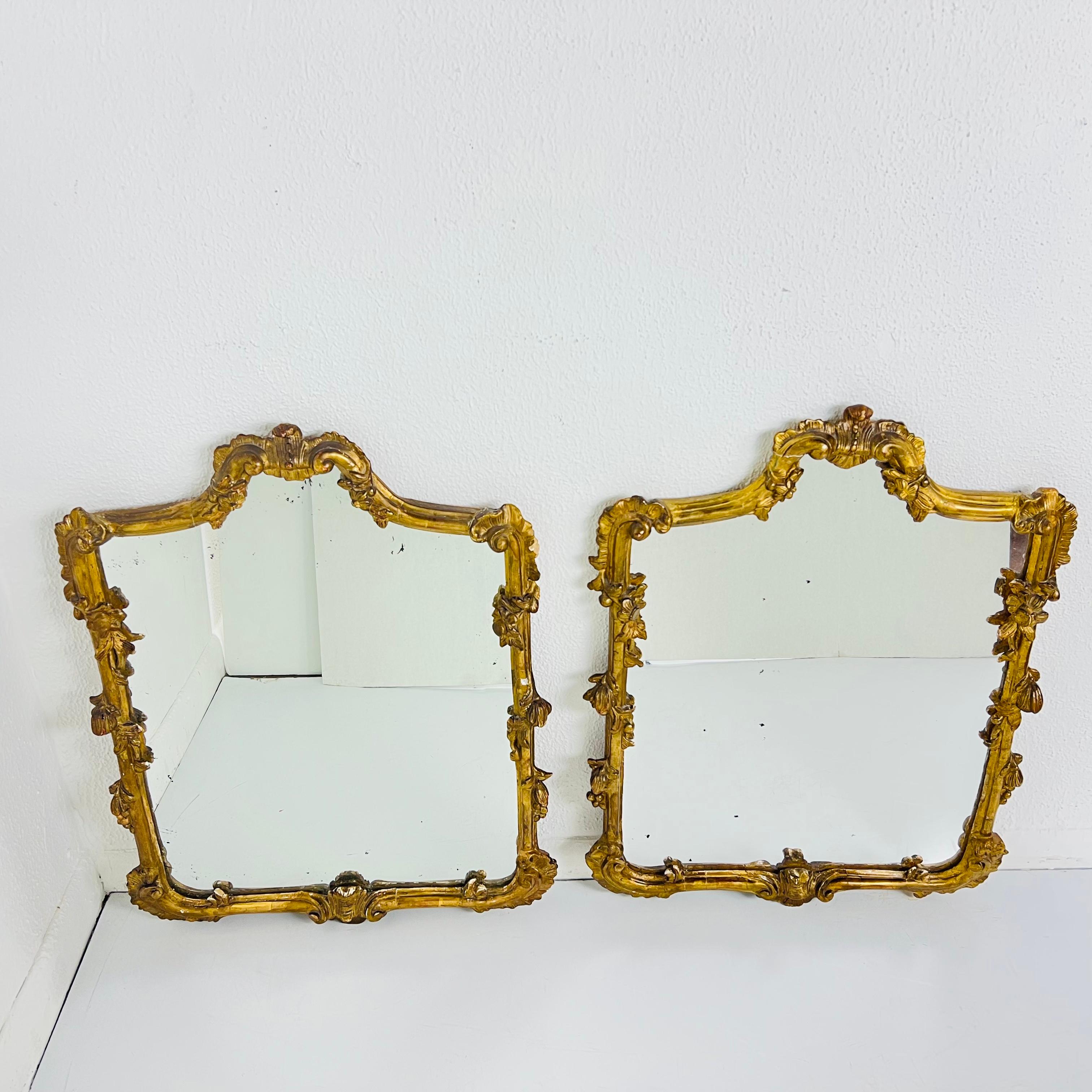 Pair of ornate vintage gilded plaster and wood wall mirrors with antiqued glass. Some cosmetic imperfections including crack at top left of one mirror and chips/dings at various spots in frames.