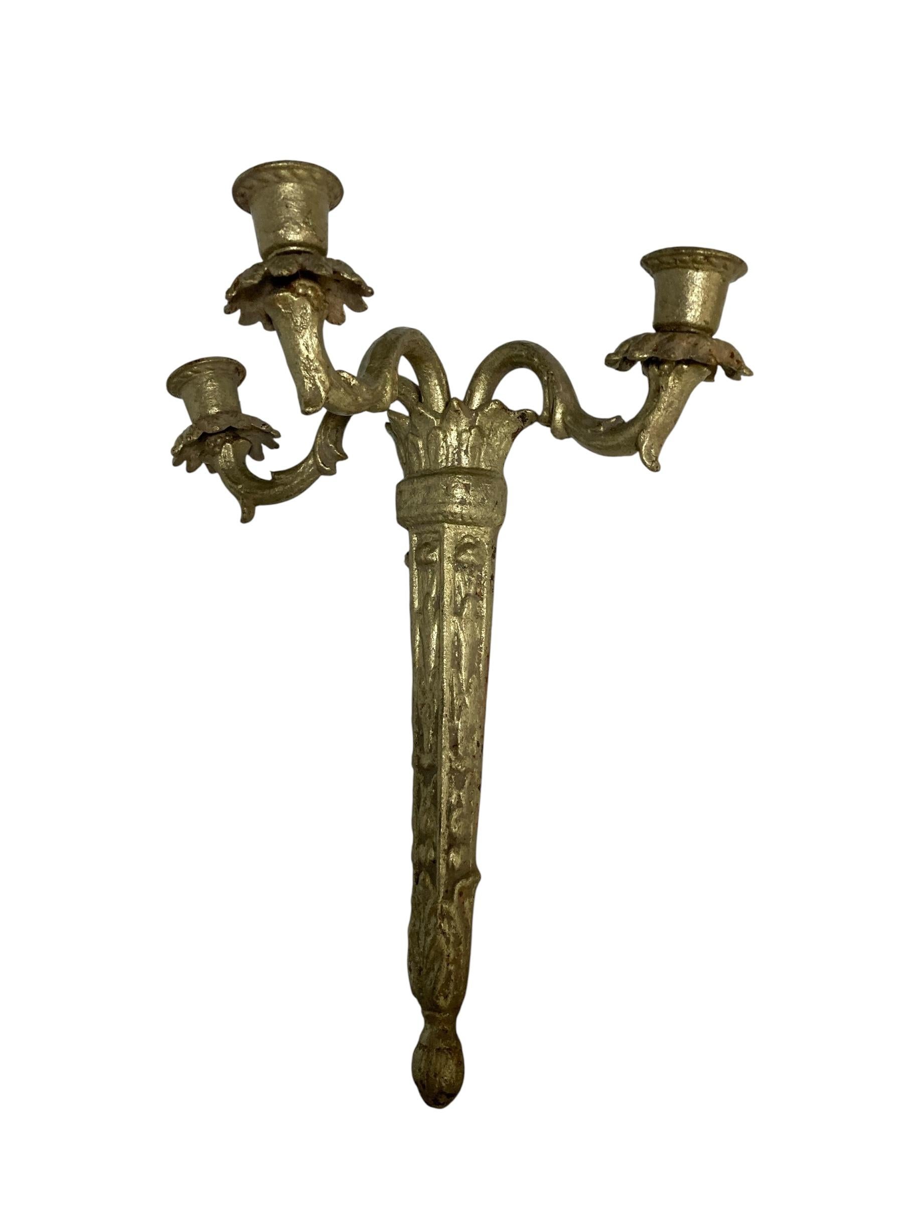 Paar verschnörkelte Wandleuchter aus Gusseisen mit Gold Finish. Jede hat drei Kerzenhalter.  Die Arme der Leuchter sind beweglich und können so in die richtige Position gebracht werden. Natürliche Patina verleiht diesen wunderschönen