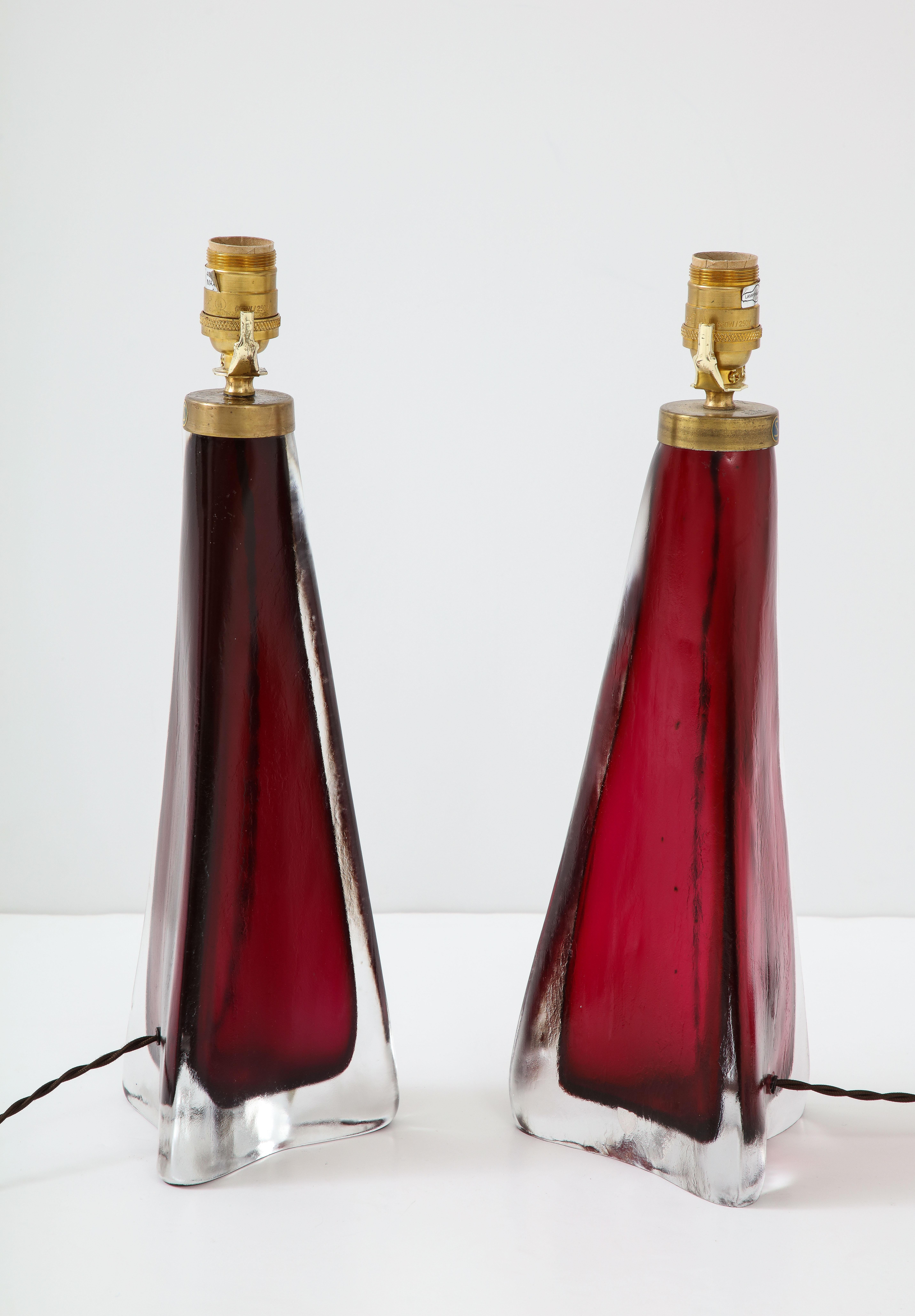 A stunning pair of Orrefors crystal lamps in a beautiful, deep shade of red with brass fittings. More than a pair of lamps, these are works of art that will add a touch of glamour to a space.