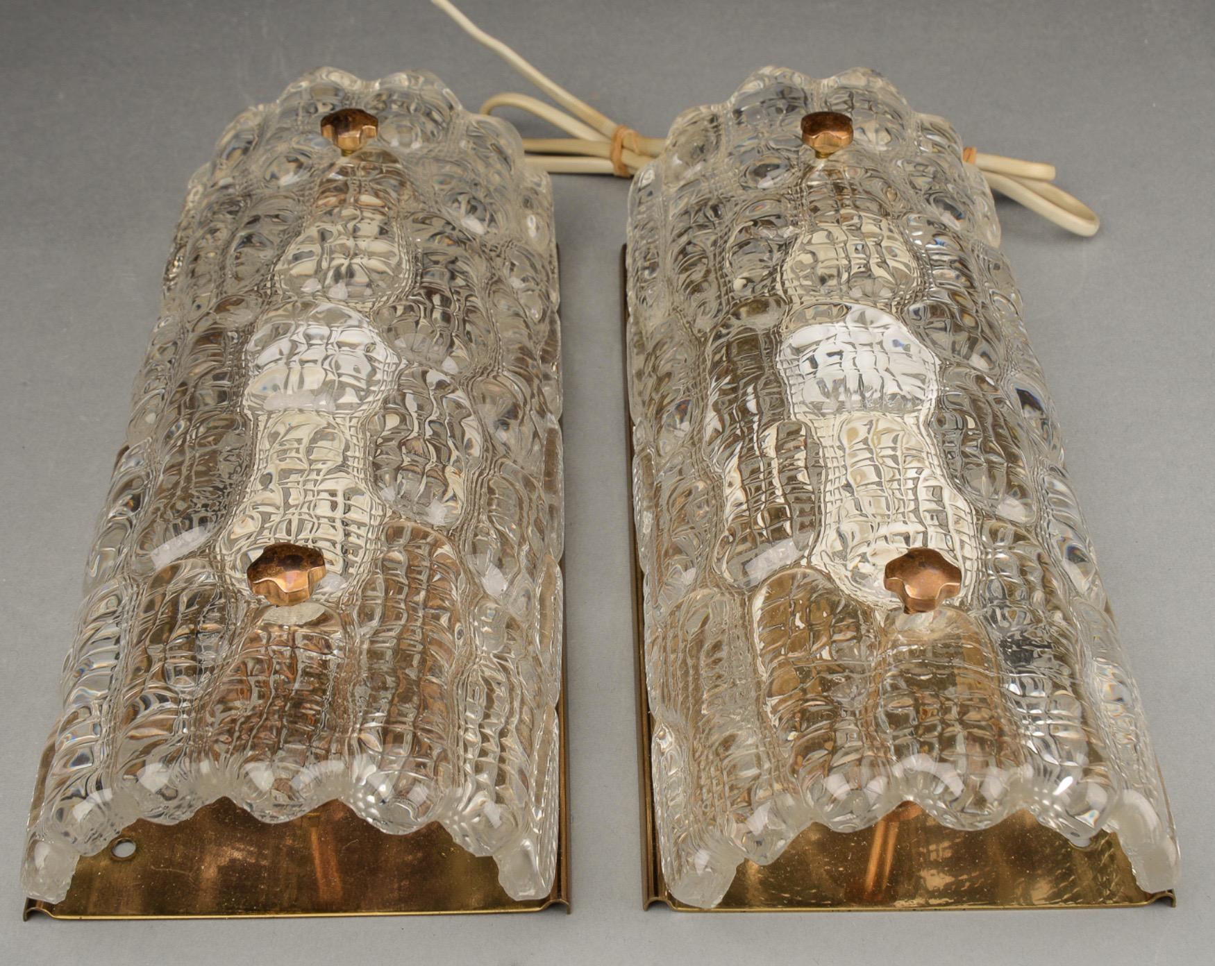 Pair of Orrefors clear colored glass sconces, crocodile pattern, glass shades are resting on a brass frame with brass fasteners.
These also come in a warm amber toned glass.
Hold one candelabra bulb each.