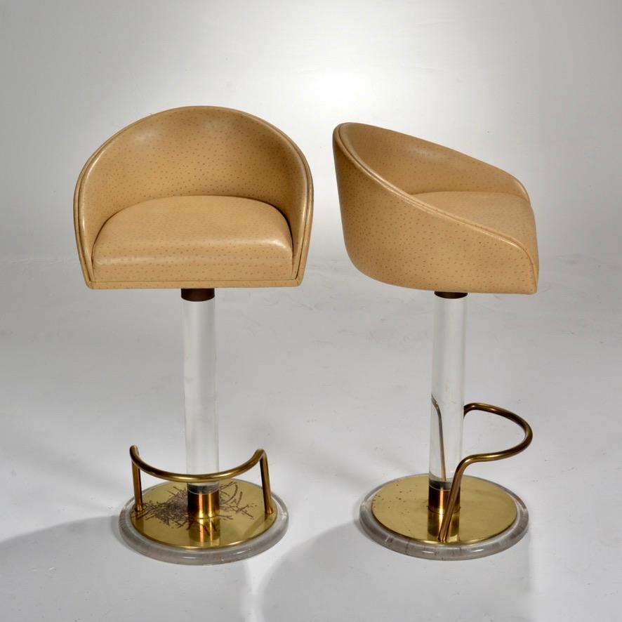 Amazing pair of ostrich leather, Lucite, and brass swiveling bar stools with footrests, designed and signed by Lion in Frost.