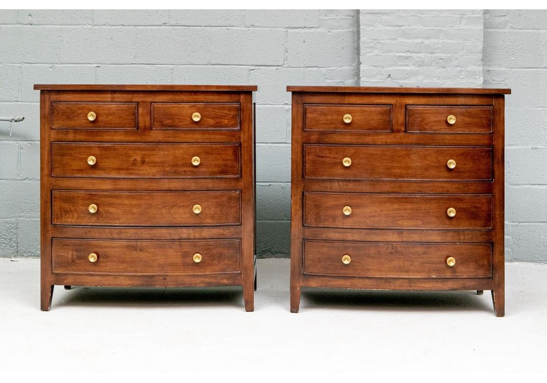 A pair of very well made two-over-three bow front chests in a medium dark stain with an elegant high polish. Two short over three long drawers with incised molding lines and brass knob pulls. Recessed sides and raised on slightly splayed front legs