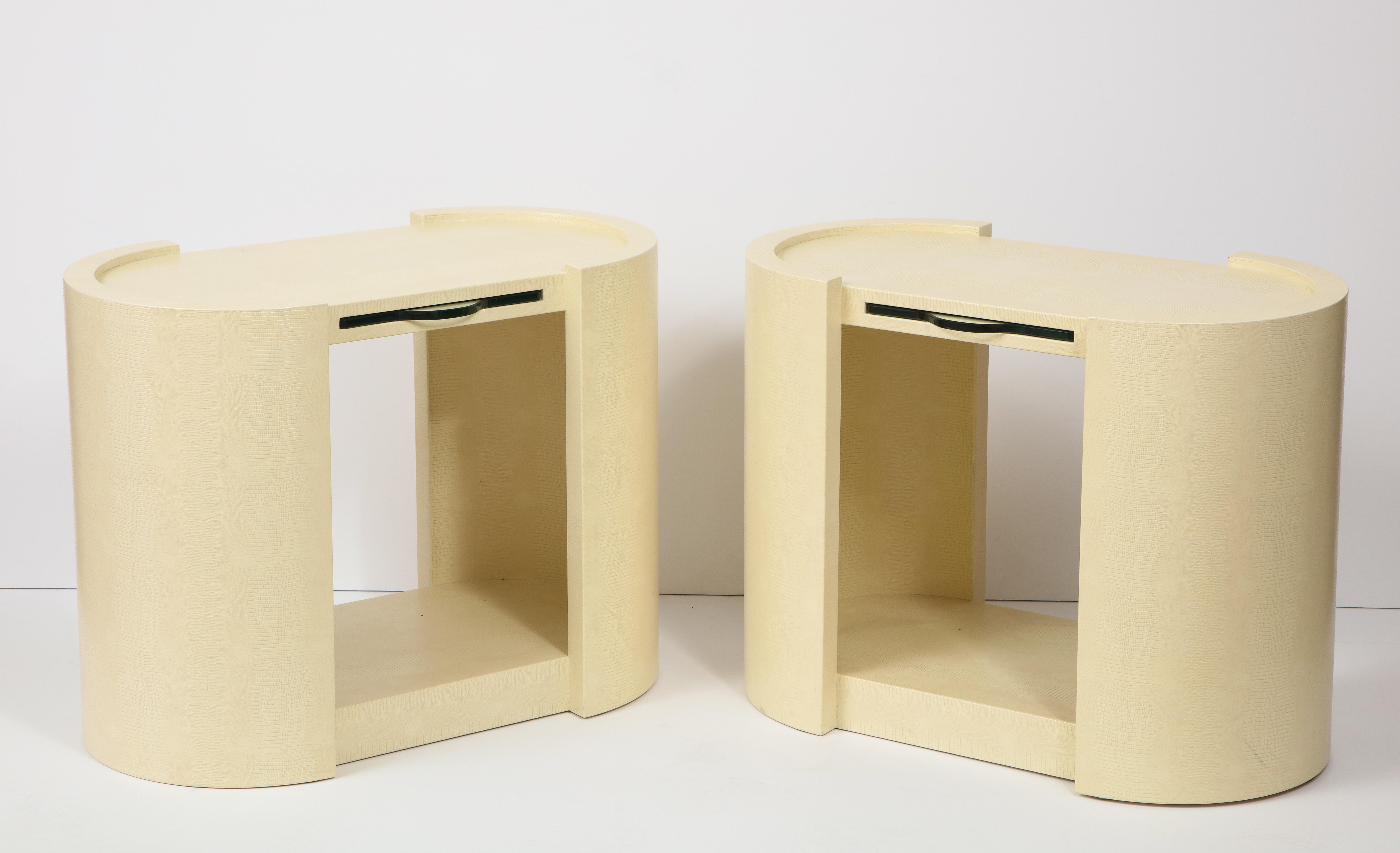 Pair of cream colored embossed leather side tables / nightstands by Karl Springer, 1982.
The oval tables have glass pullout / pull-out trays and on the bottom there are adjustable feet and
the Karl Springer label.
 