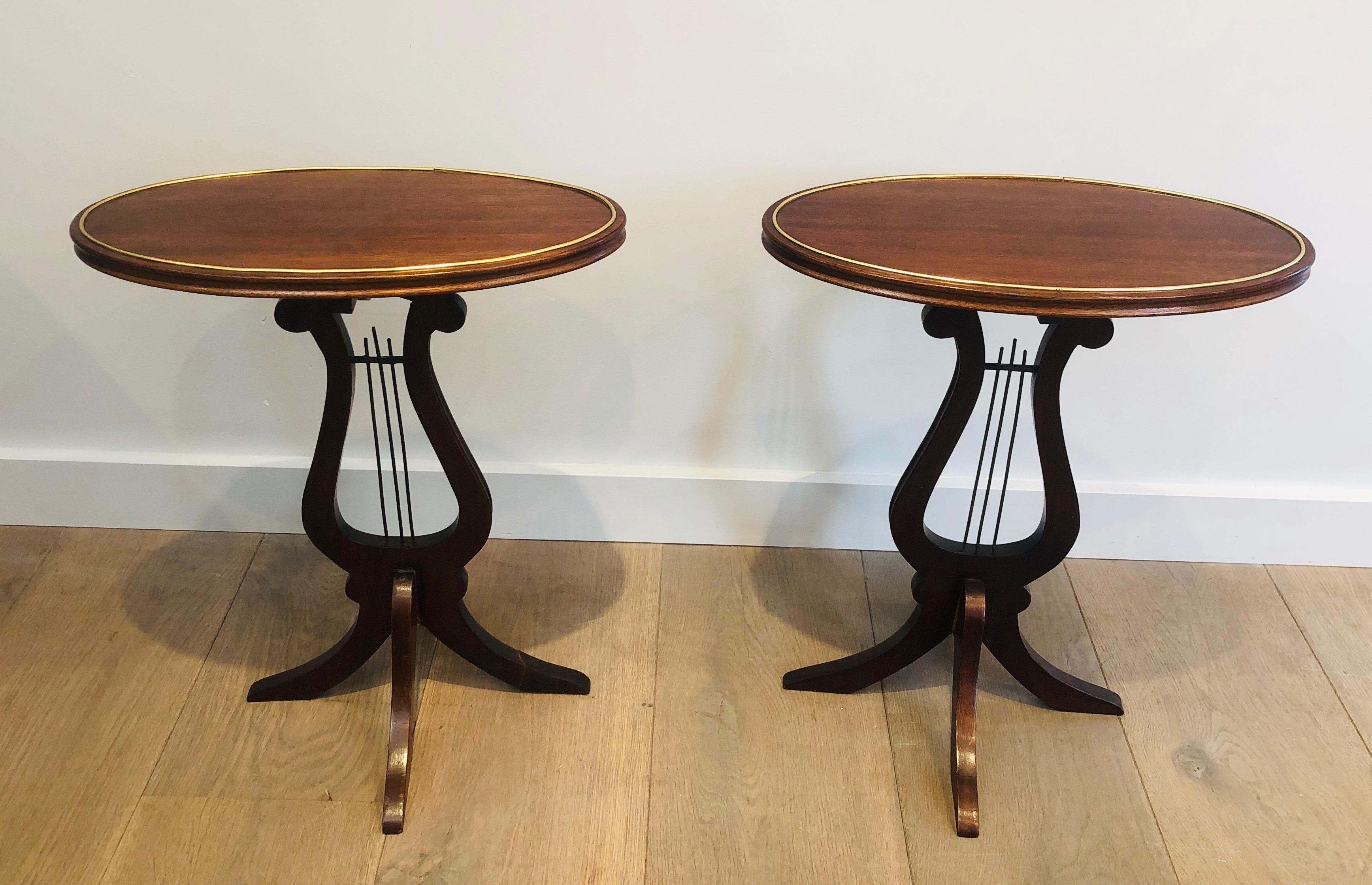 This pair of oval lyra side tables or martini tables is made of mahogany with brass nets. One of the leg has been restored as it can be seen on the pictures. This is a French work, circa 1960.