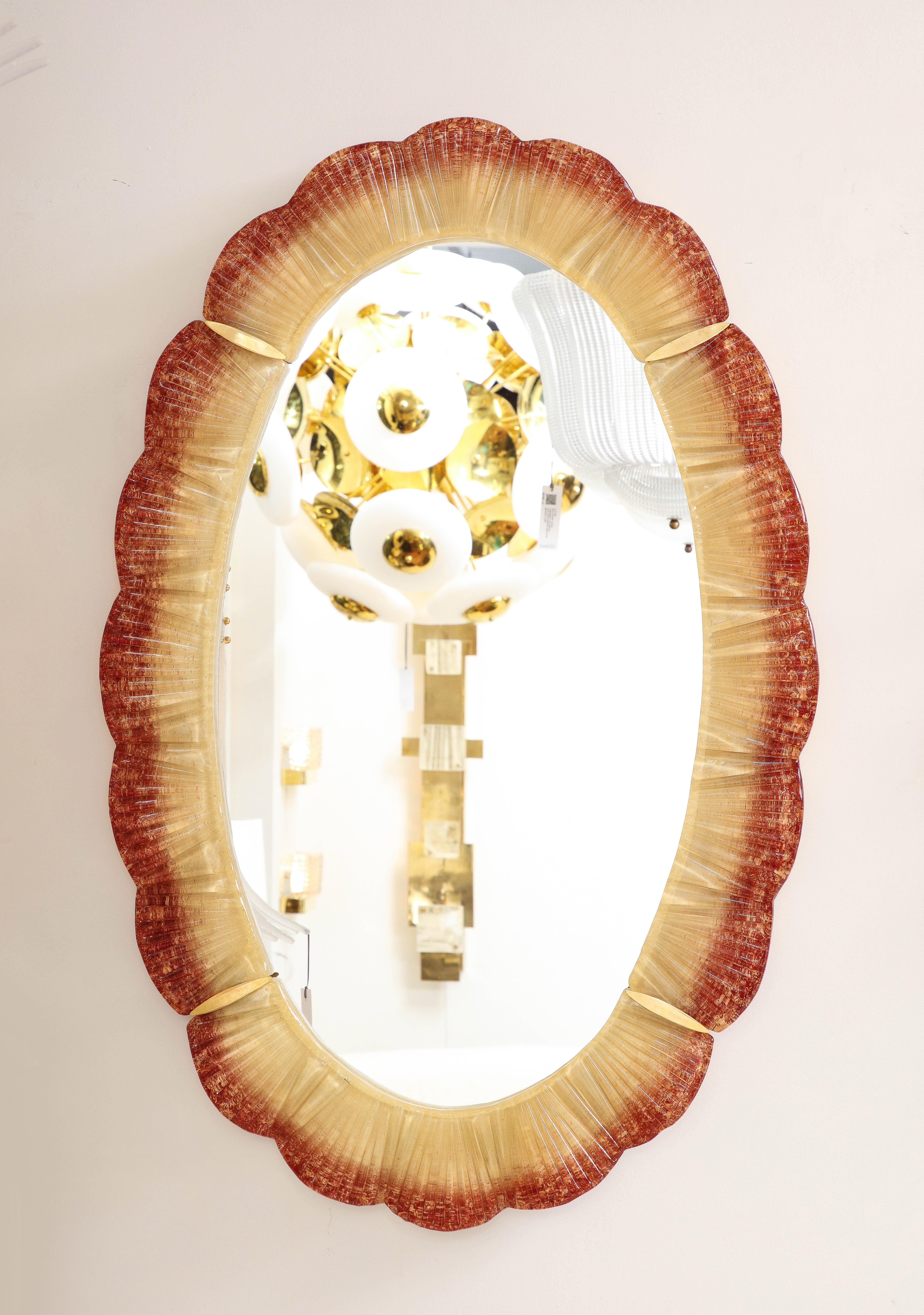 Pair of Oval Scalloped Murano glass and brass mirrors in an orange-red amber and gold color. Individually hand-casted sections of Murano glass with a scalloped edge in a dramatic ombre tone of orange-red to gold amber are united to form an oval