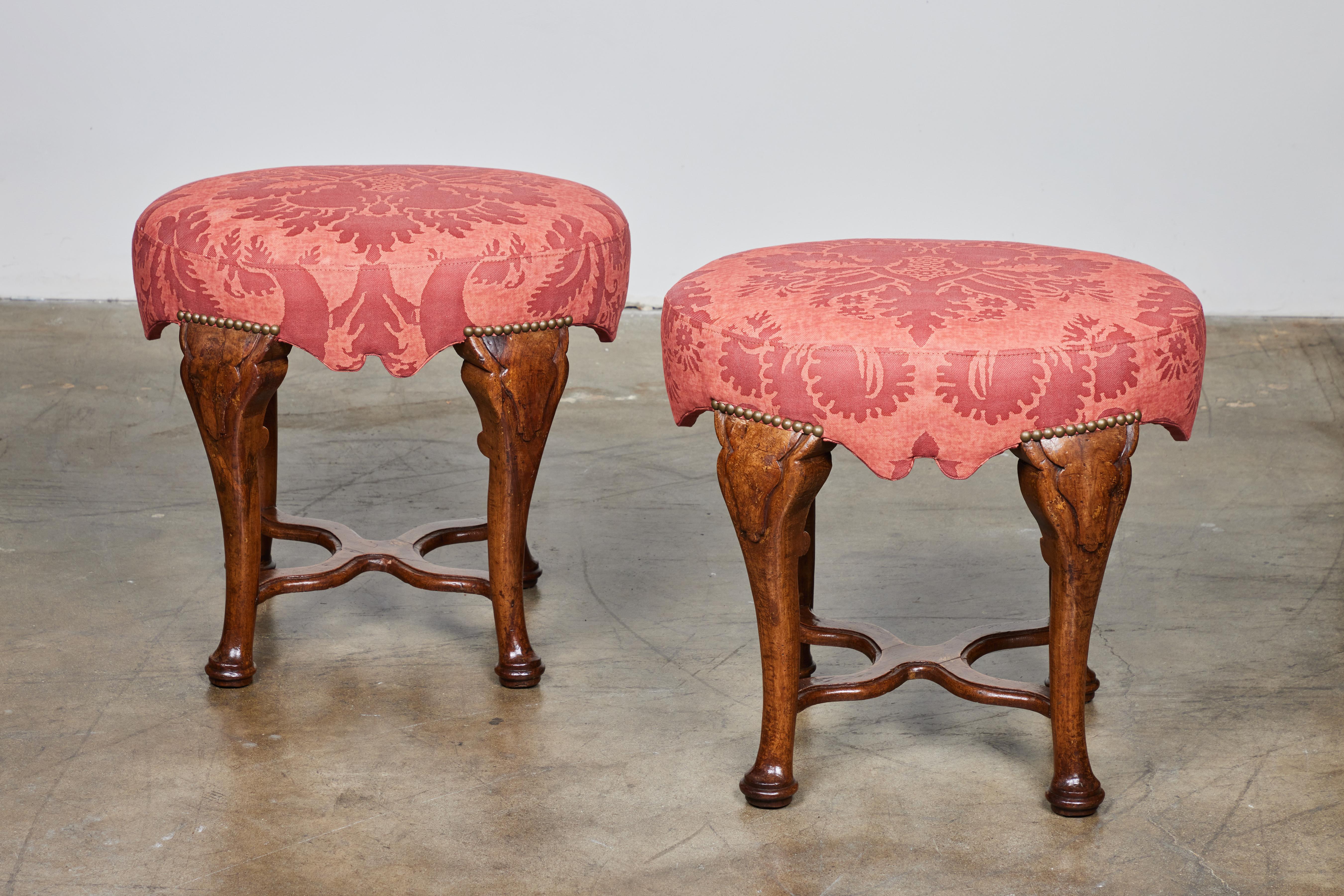 Pair of hand carved walnut oval stools with X stretchers. New Fortuny upholstery.