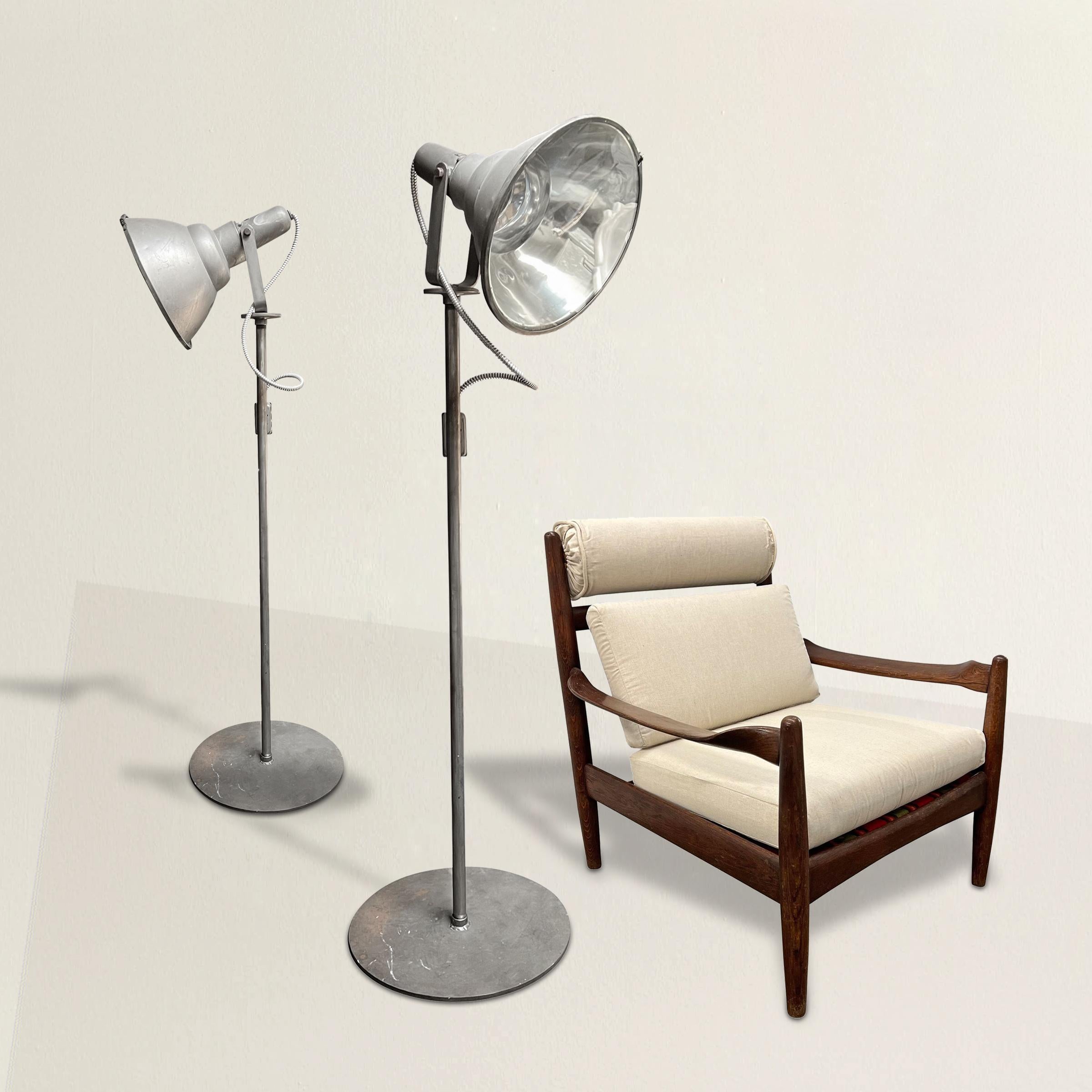 An impressive pair of 20th century American industrial oversized floor lamps with large swiveling heads mounted on steel posts with wide round bases. Newly re-wired with dimmer switches for residential use. The perfect lamps for your city loft