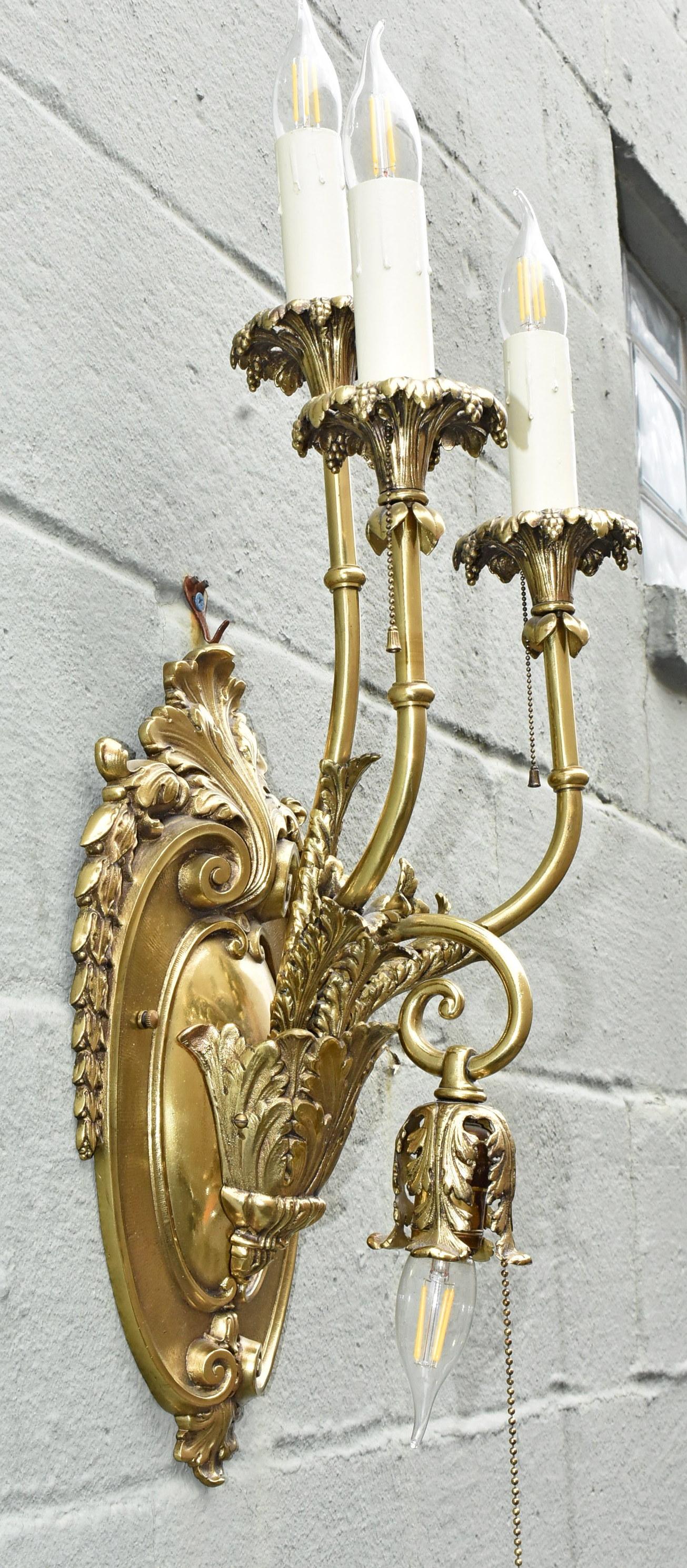 Pair of Oversized Brass French Sconces with Four Arms. Circa Early 20th Century. Detailed brass sconces with three arms up and one arm down each with a pull chain. Rewired and in excellent condition consistent with usage and age. Large back plates
