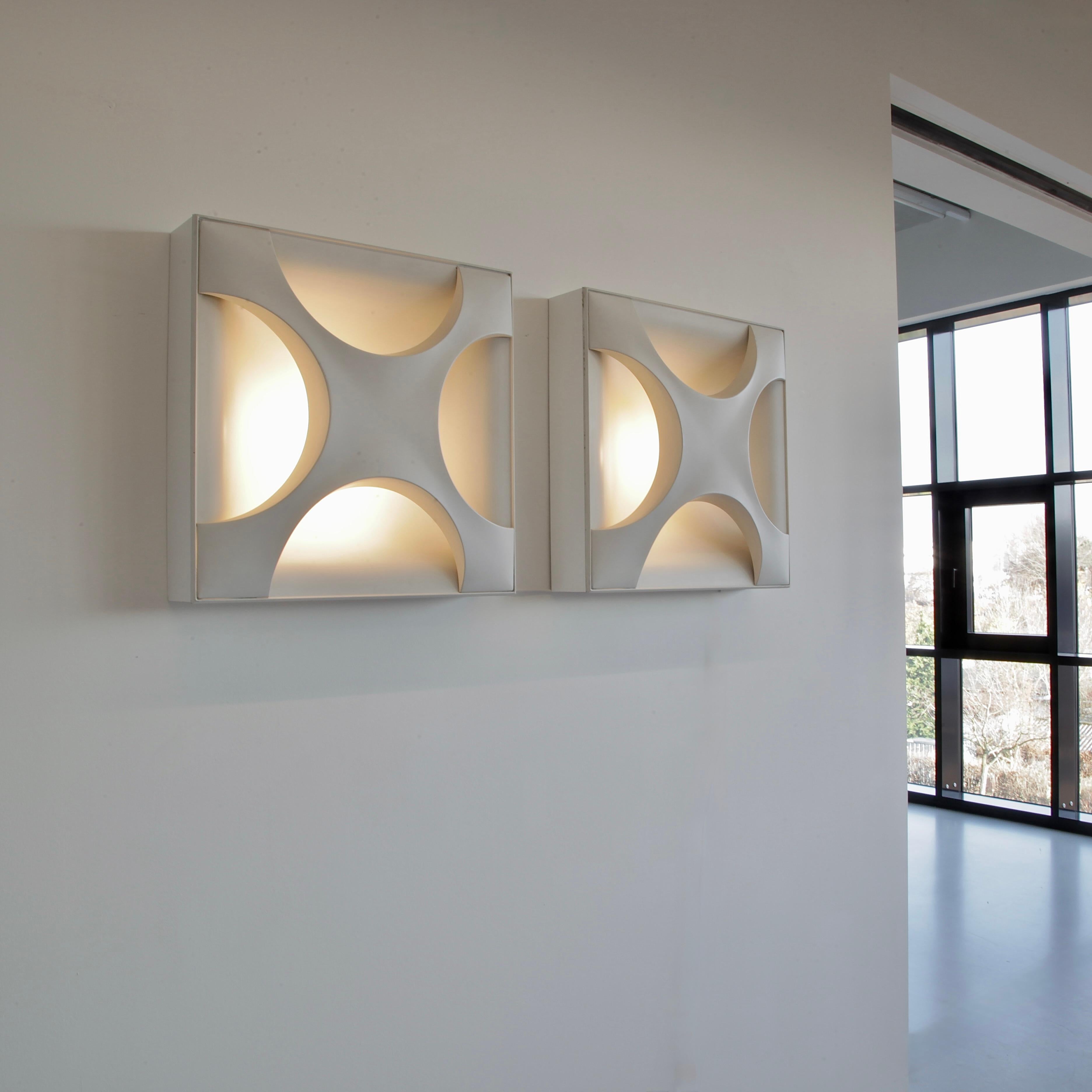 Zwei große quadratische Wandleuchten mit je vier E27-Leuchtmitteln, die hinter einem lackierten Metallsteg verborgen sind. Dadurch entsteht ein tiefes dreidimensionales Licht. Dieses Modell wird von der Staff Lighting Company als 'Kreuzaustern'
