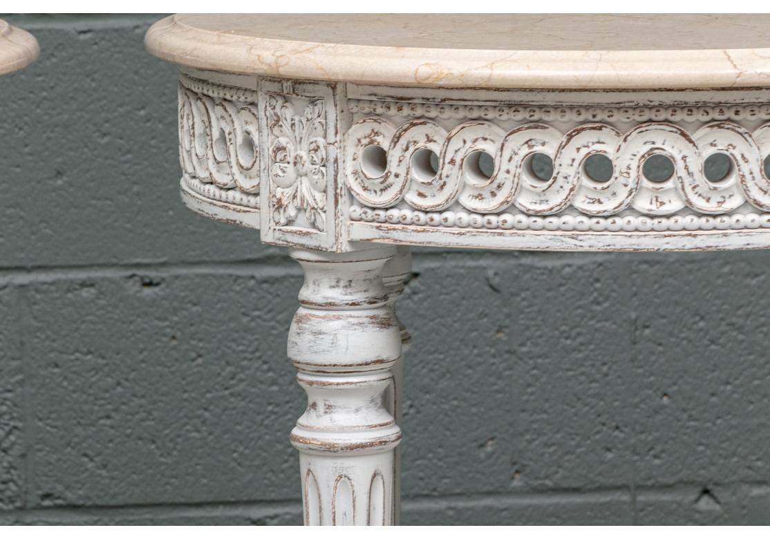 Pair of paint decorated round side table with pierced geometric motif and intentionally distressed finish. The table with fluted legs that are conjoined with an X-form stretcher and covered with compatible marble tops. There is a slight Size