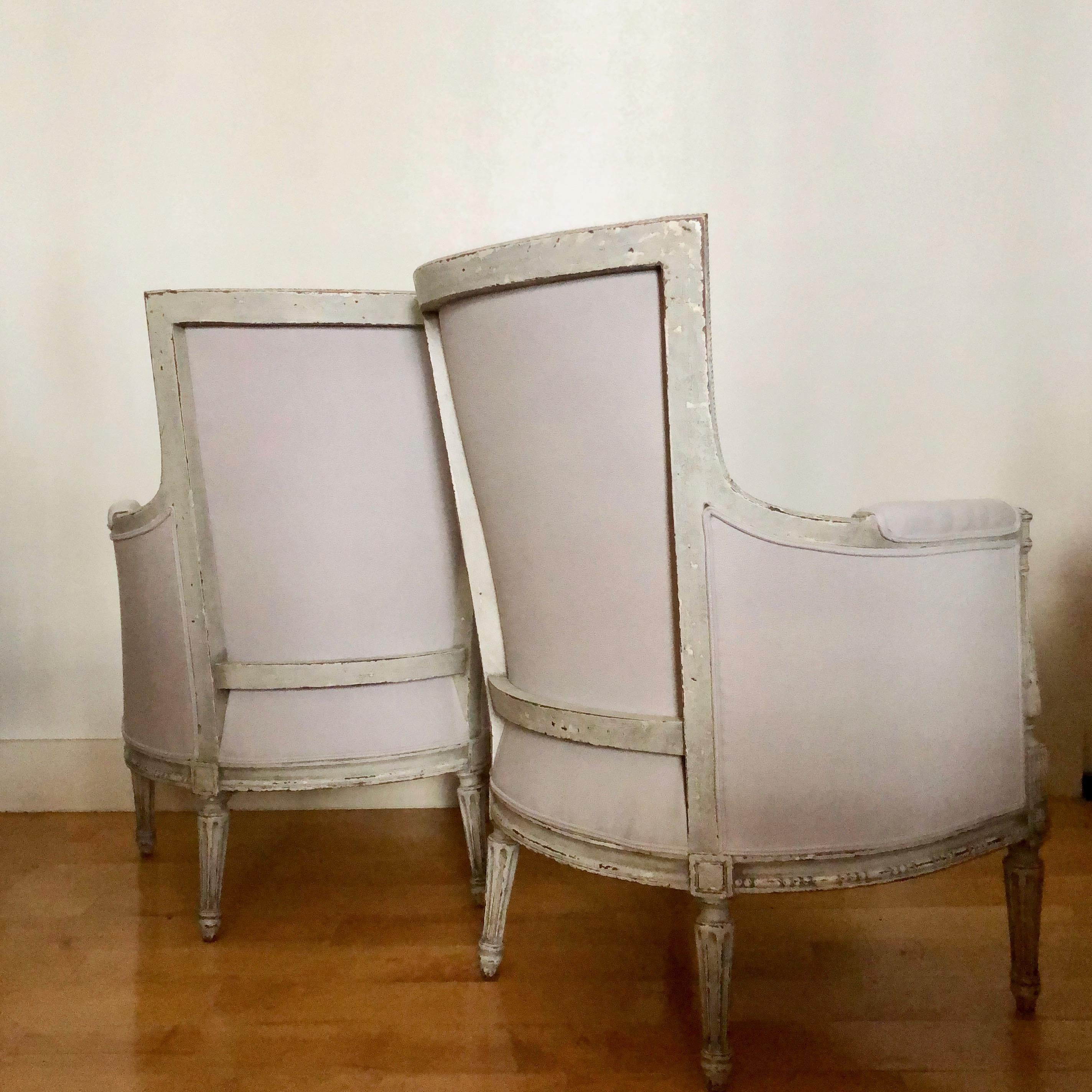 A pair of painted 19th century French Directoire style bergères. The horned backs (à cornes) are coved with side and top rails that curve inward to create horns at the corners and terminating in scrolls, the armrests consoles baluster shaped, the