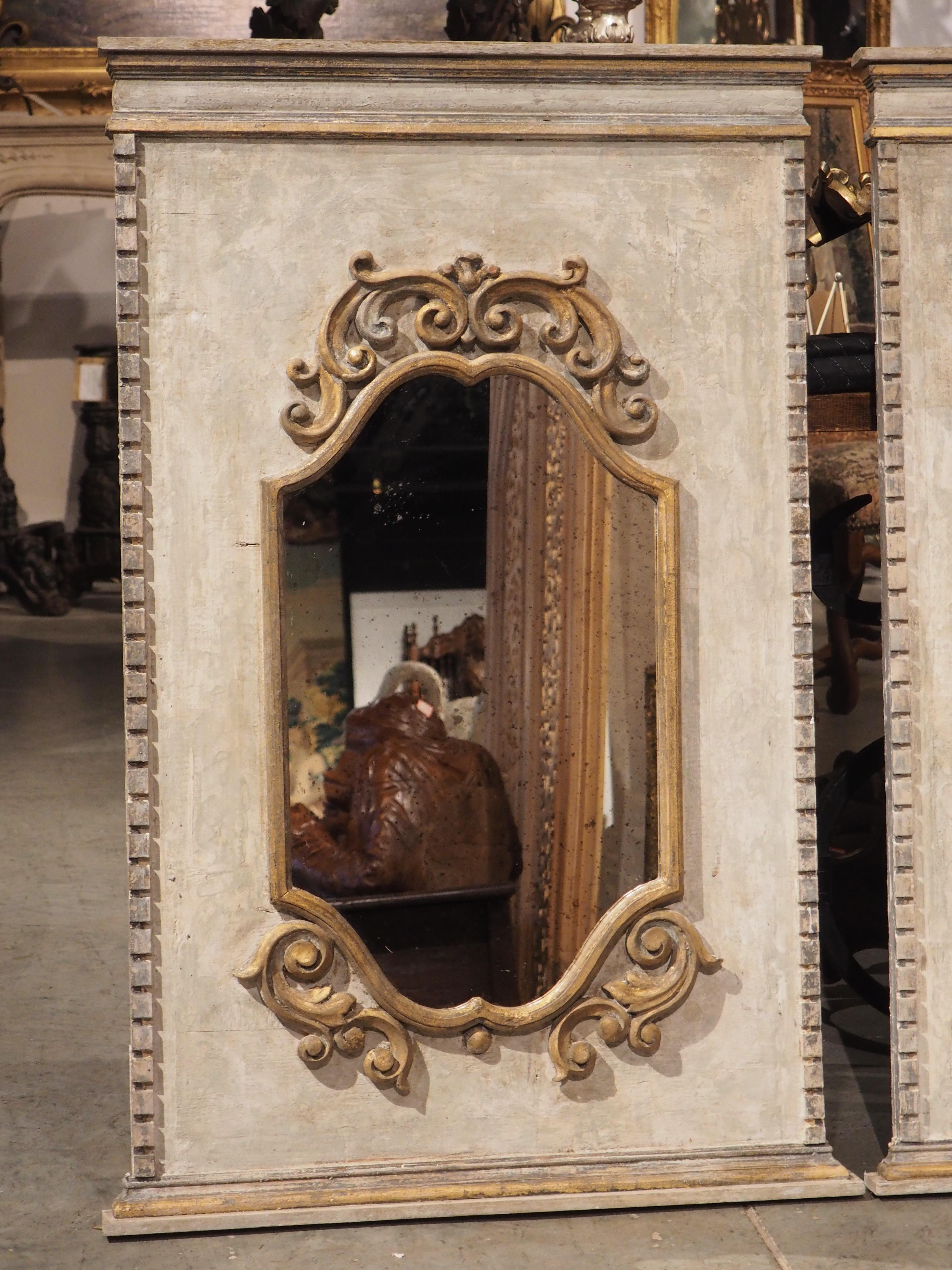 Hand-carved in Florence, Italy, this pair of wall mirrors have been surrounded by giltwood carvings on top of painted boiserie panels. The panels, which feature a column of crenellation along each edge, have been painted in a polychrome