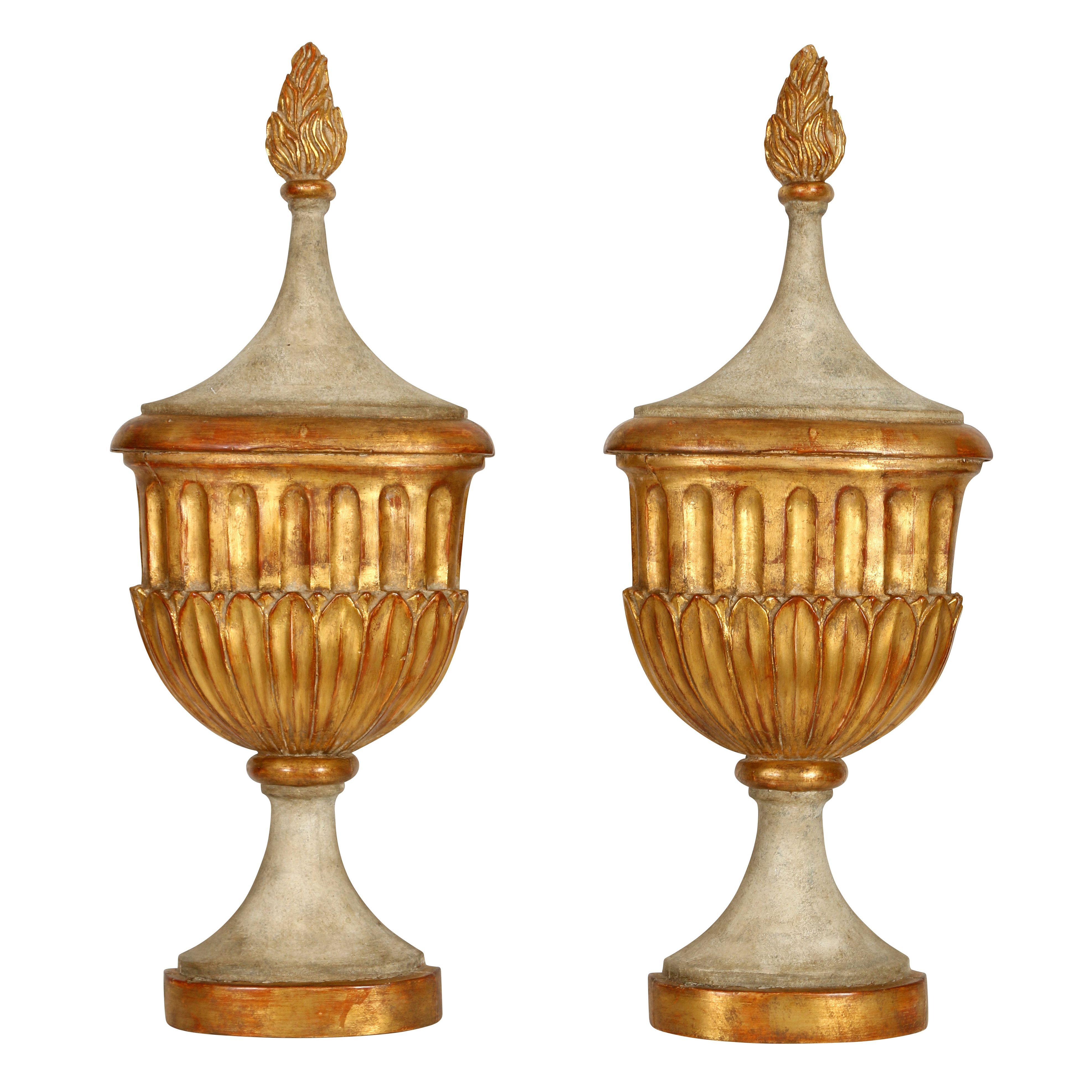 A pair of elegant painted plaster wall urns with gold leaf accents. Painted in a soft grayish white, the urns feature lovely carved detail, including a small flame at the top. This pair would look great flanking a mirror or at an entrance--a perfect
