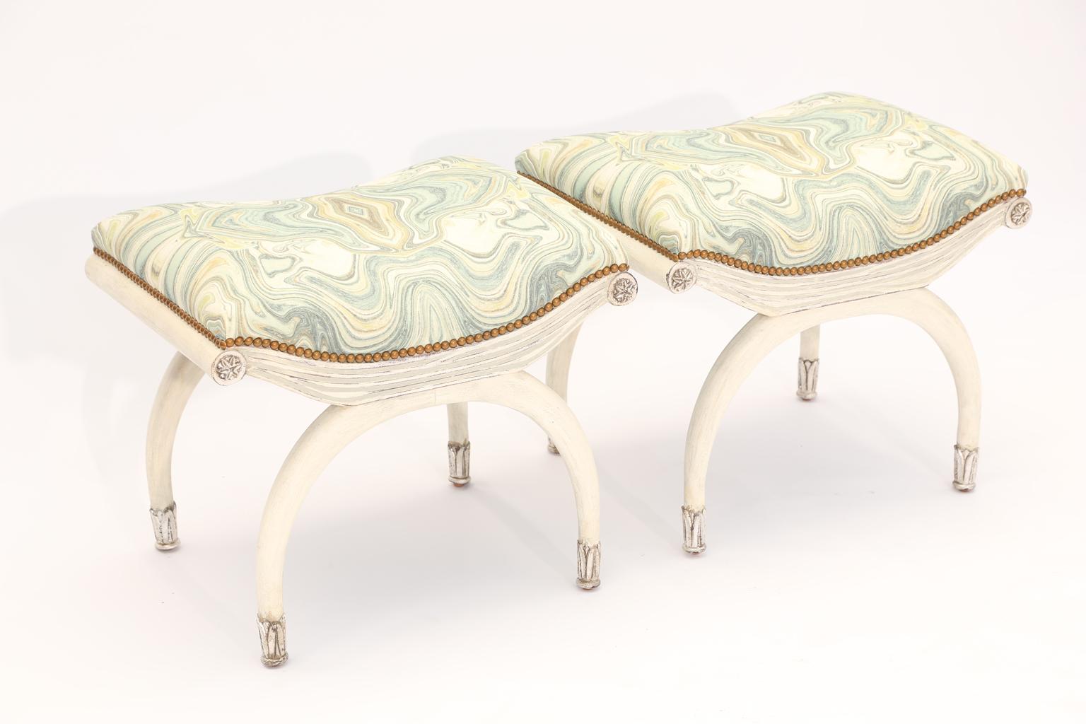 Pair of benches, each having a padded, rectangular seat, upholstered with nailheads, on painted frame with parcel silver gilt accents, the finish showing natural wear, its apron carved to resemble draped fabric, flanked by rosettes, raised on curved